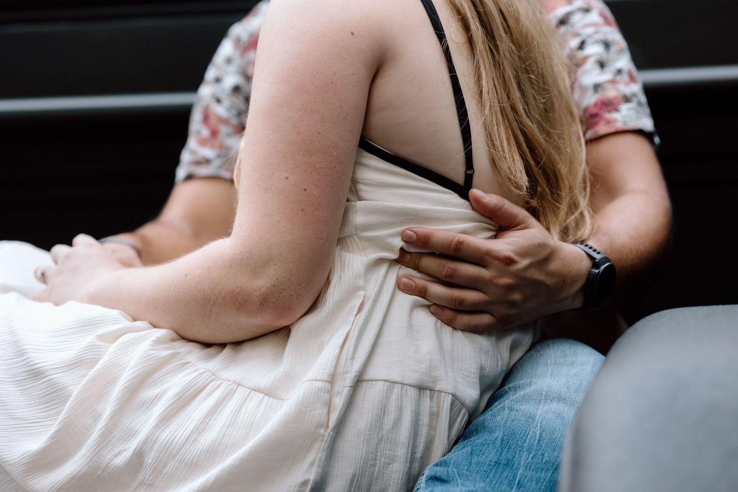 A close-up of a couple embracing, the woman in a white dress with the man's hand gently resting on her back.