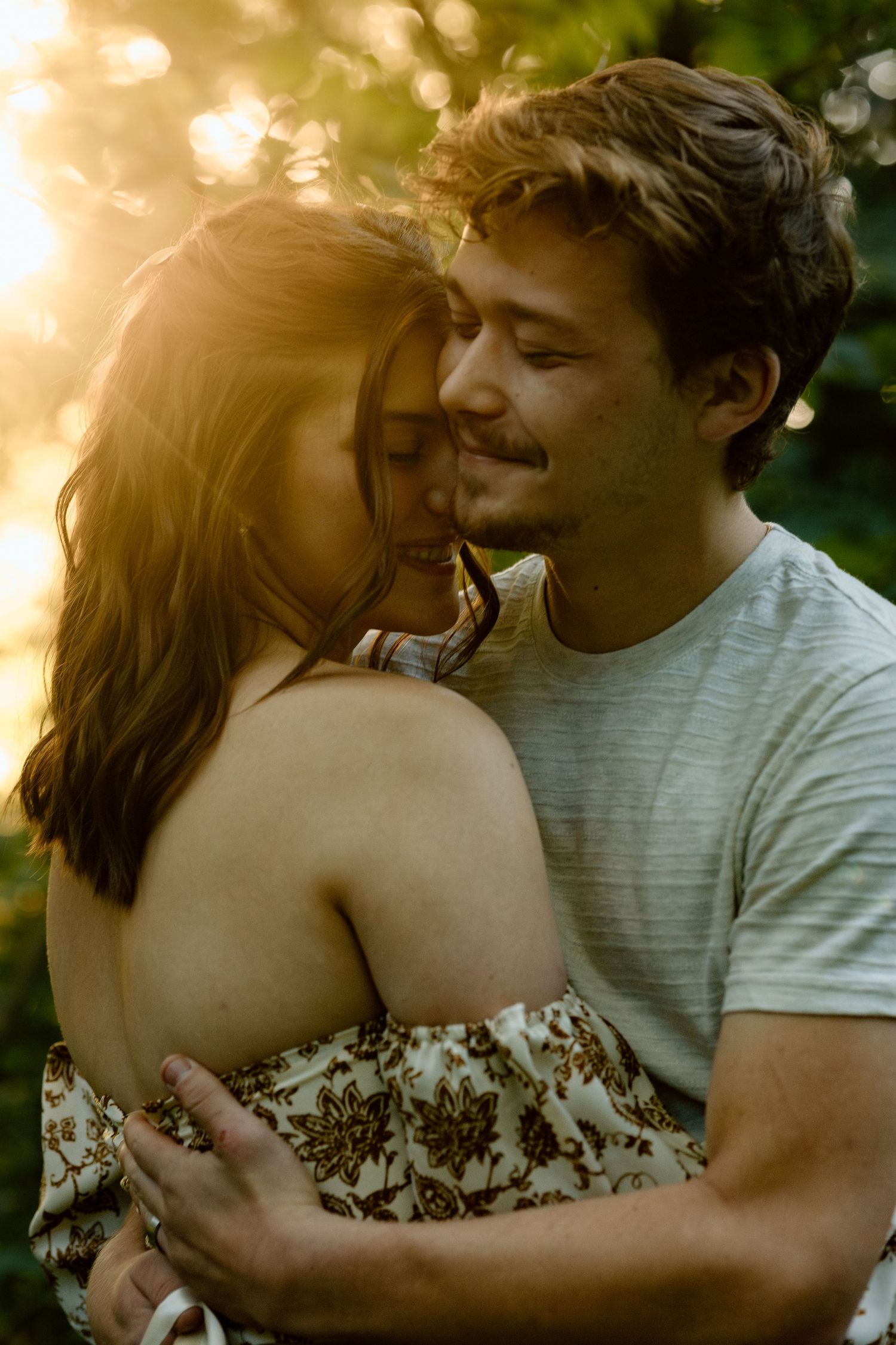 Couple embracing tenderly in warm golden sunset light in a wooded outdoor setting.