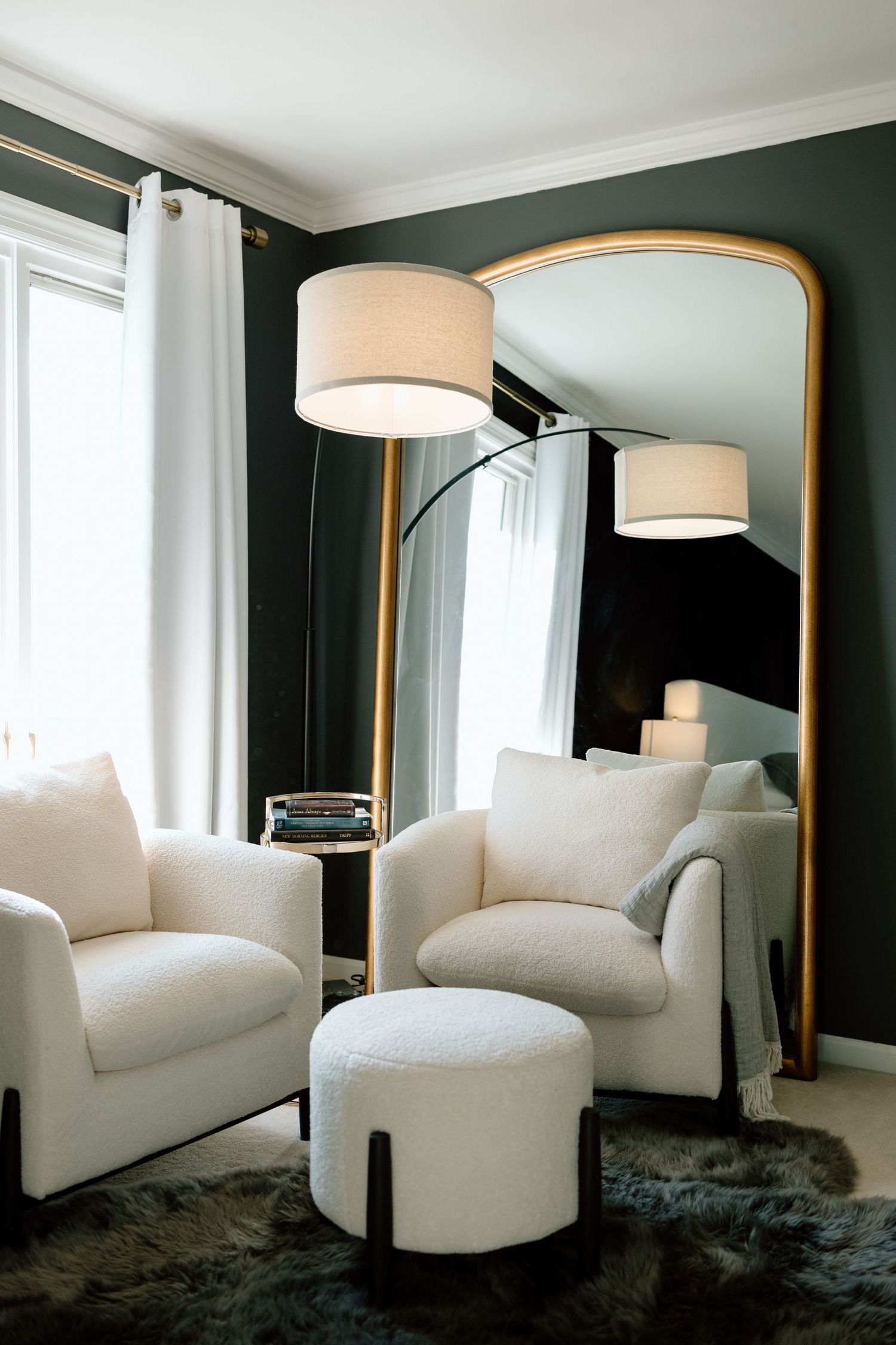 Elegant living room corner with white armchairs, gold mirror, and arc floor lamp.