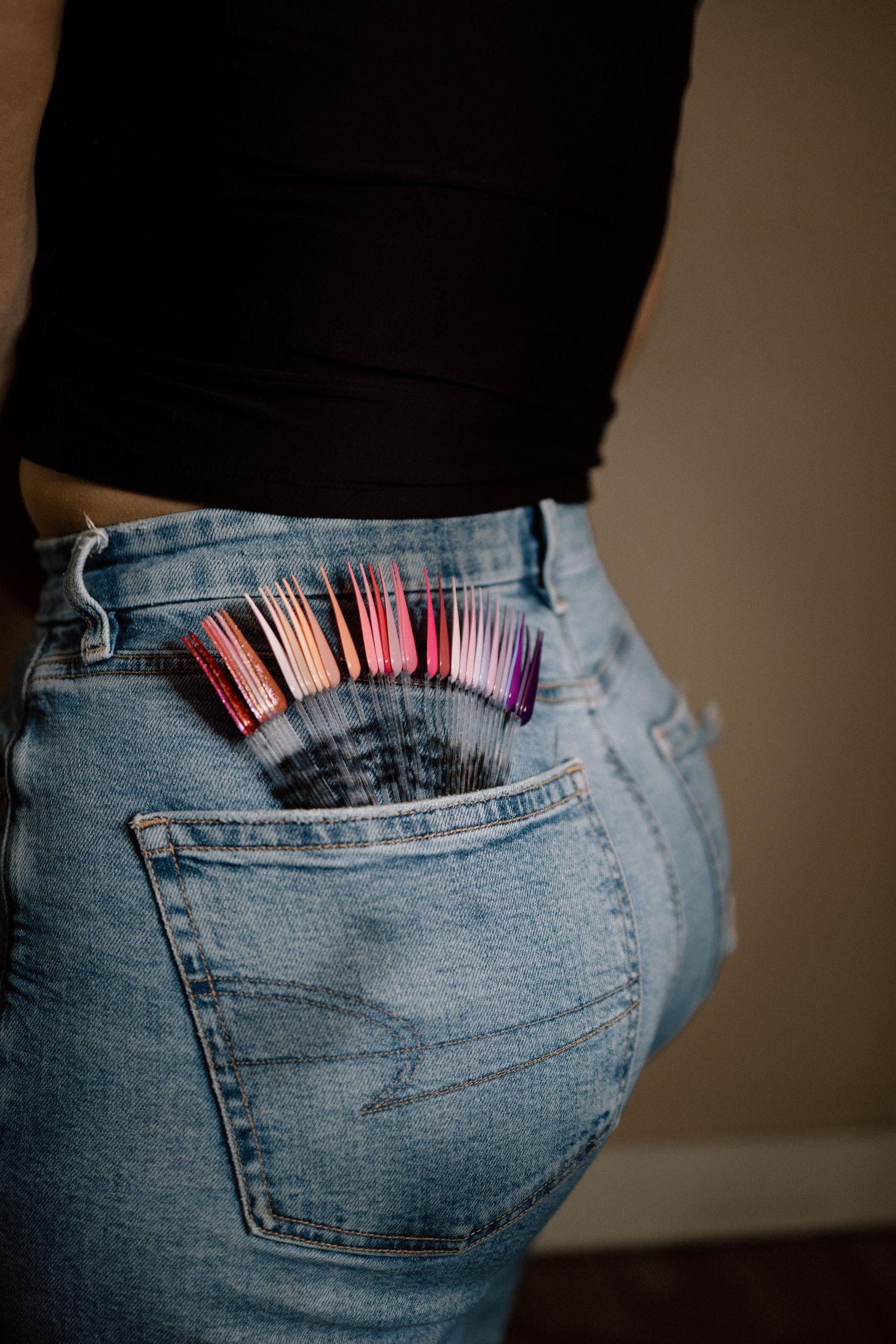 Colorful makeup brushes stored in the back pocket of blue denim jeans.