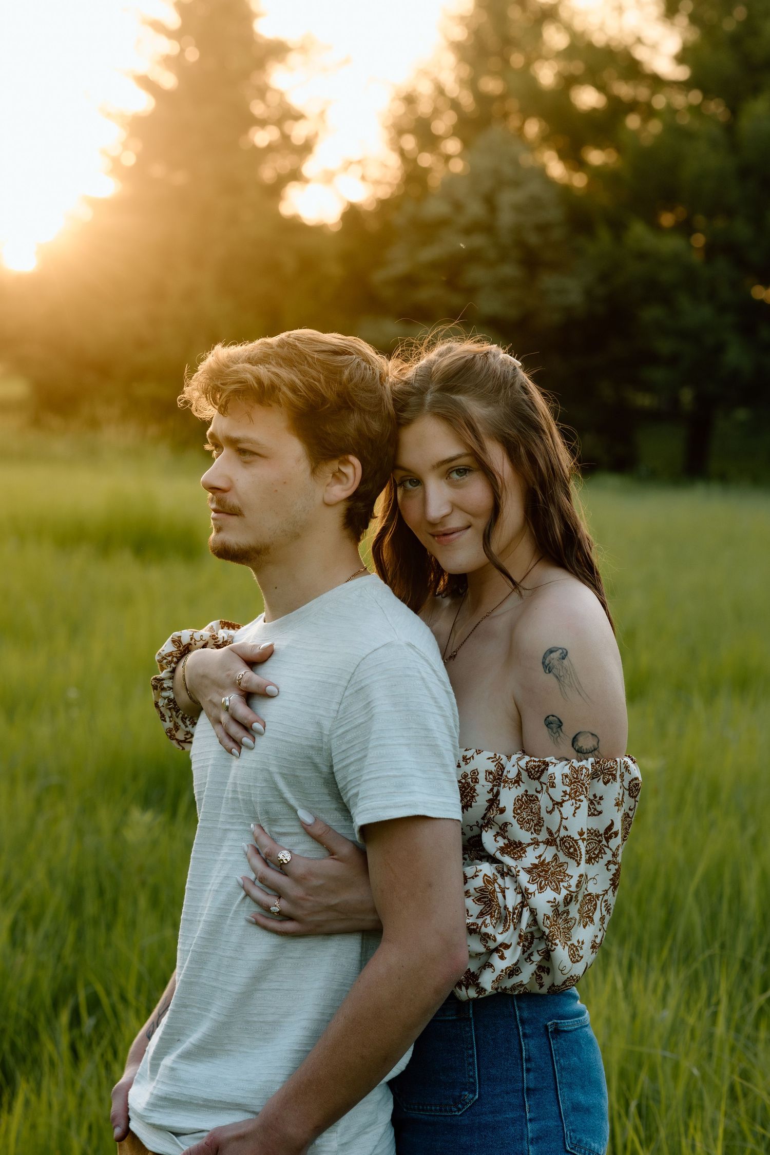 Young couple embracing in a green field during warm golden sunset light.
