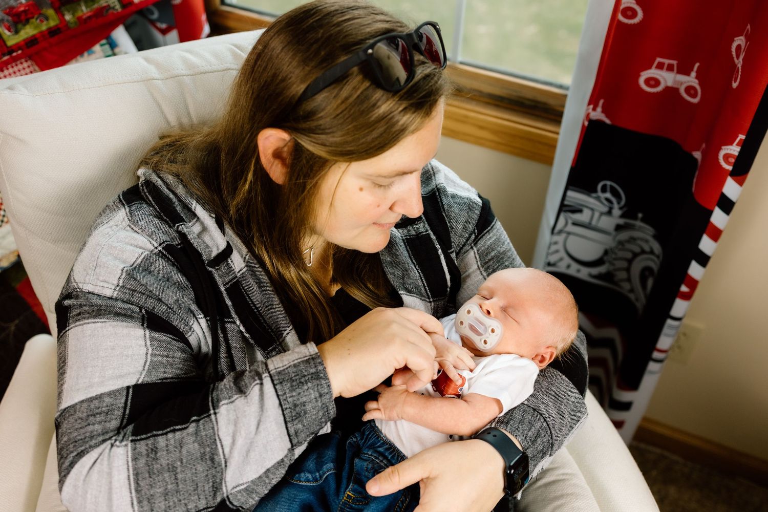 Mother in plaid shirt smiling lovingly at her newborn baby with a pacifier.