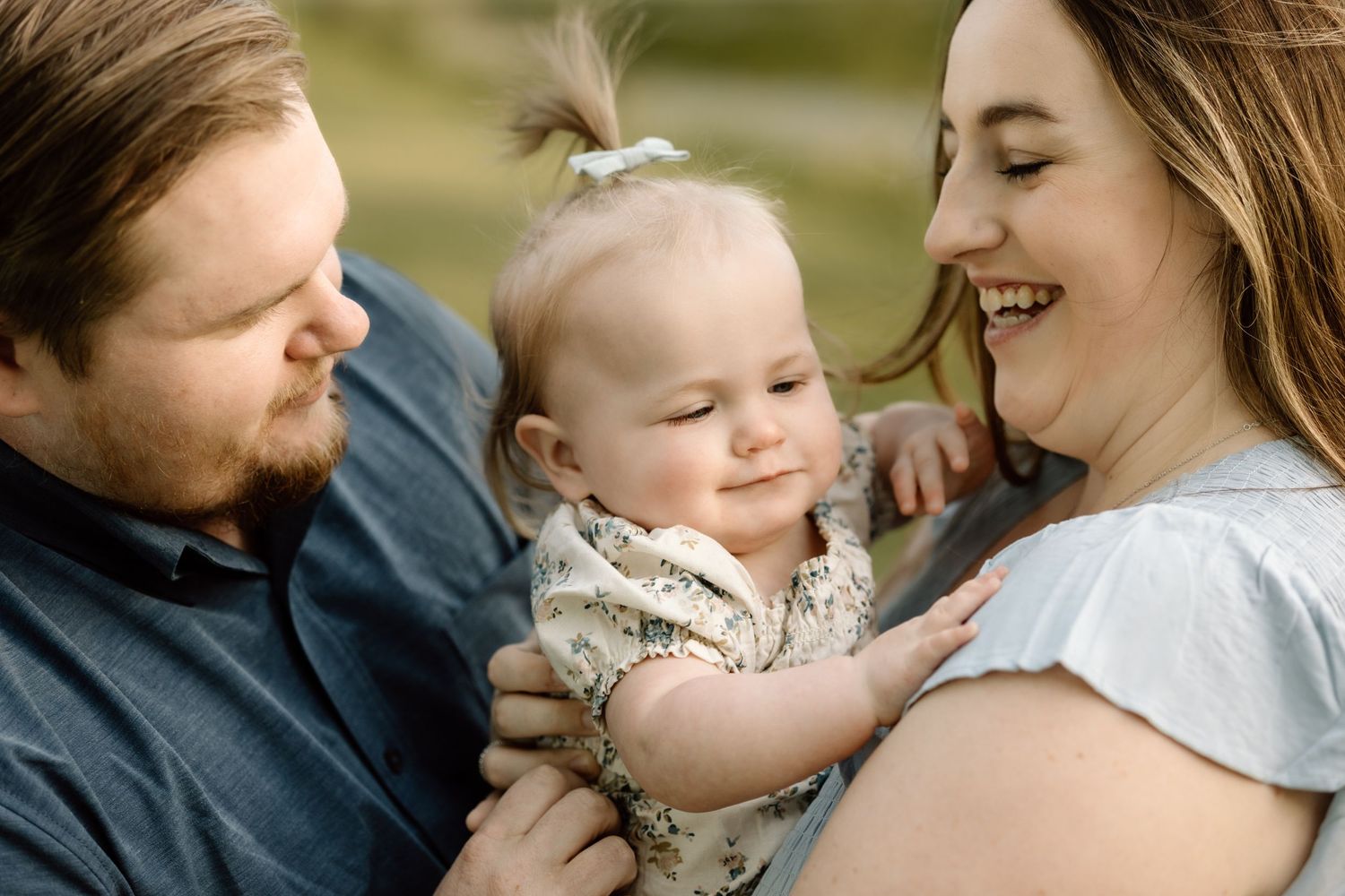 Two loving parents share a tender moment smiling at their content baby girl in a close-up outdoor portrait.