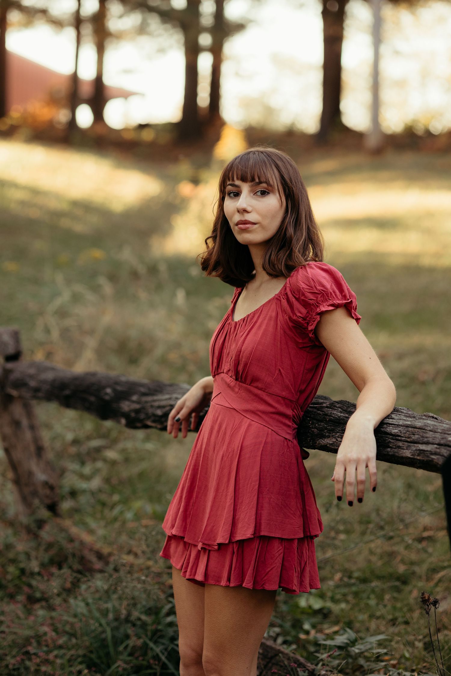 Young woman in red mini dress leaning on a wooden fence at sunset.
