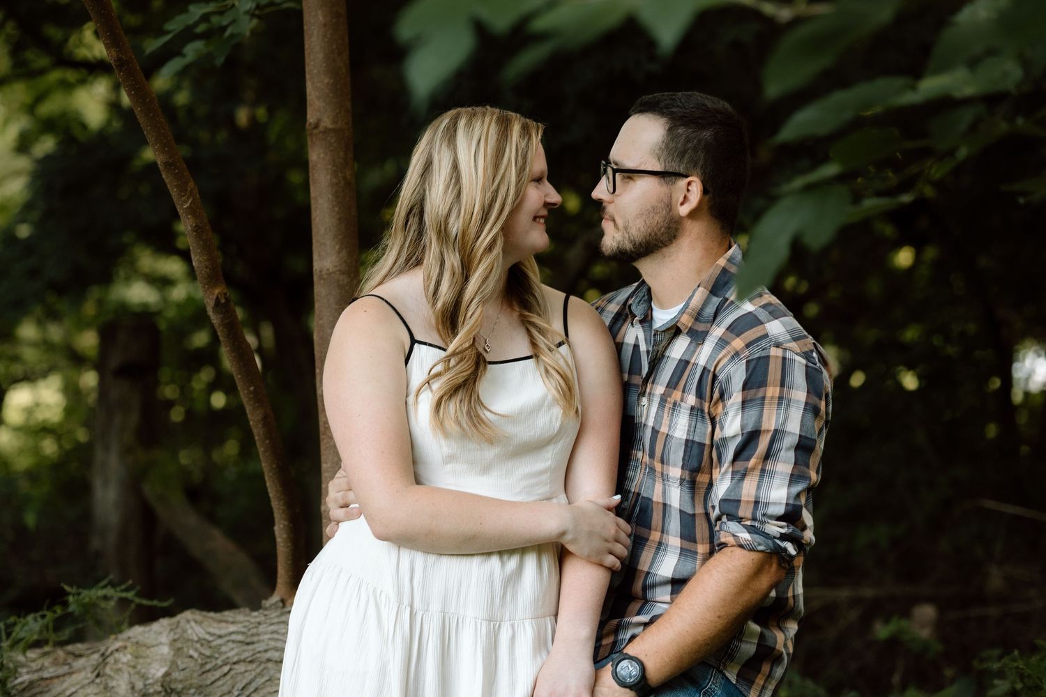 A couple gazes into each other eyes while embracing in a lush green outdoor setting during an engagement photo shoot.