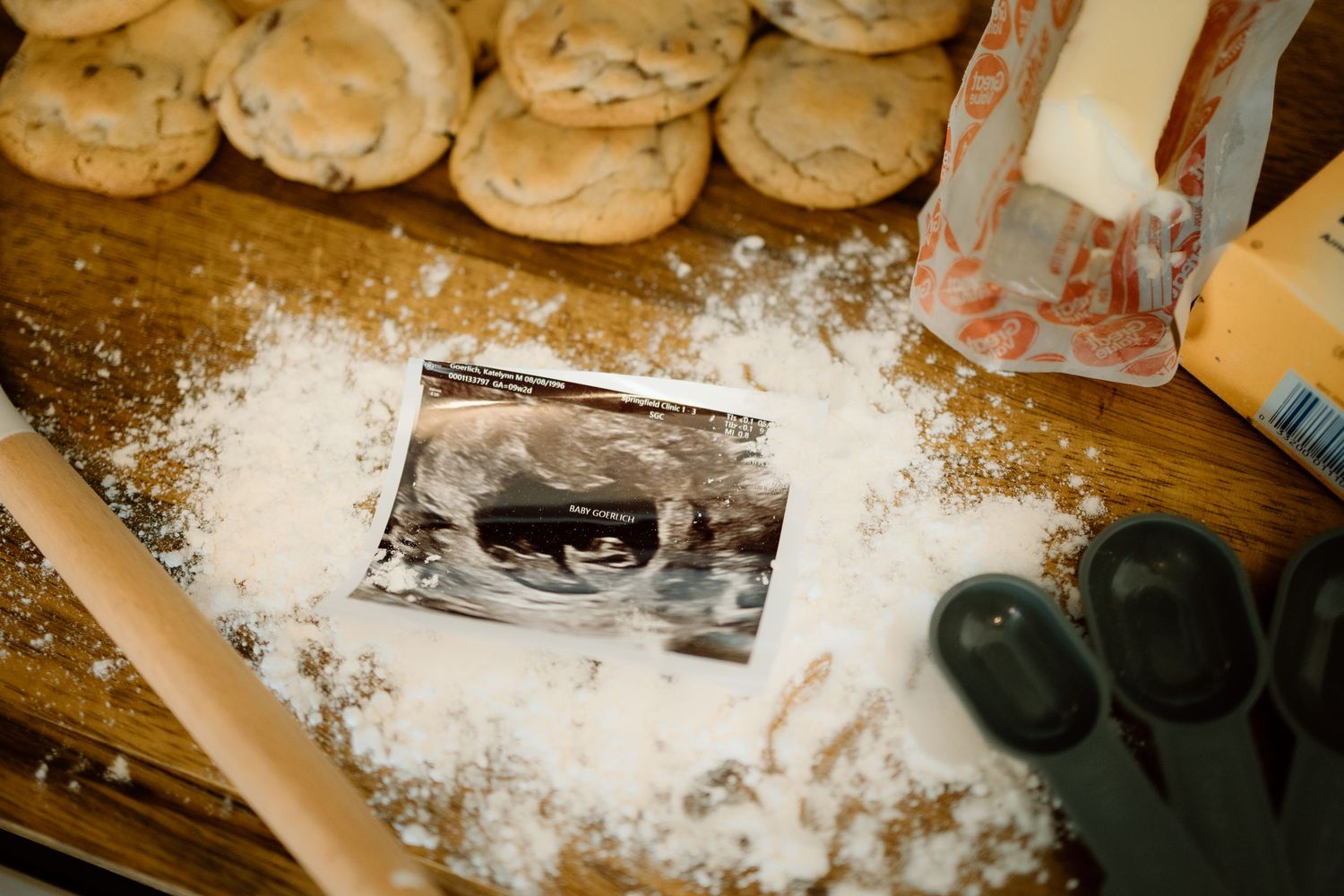 Ultrasound photo placed on flour-dusted wooden board surrounded by fresh baked chocolate chip cookies.