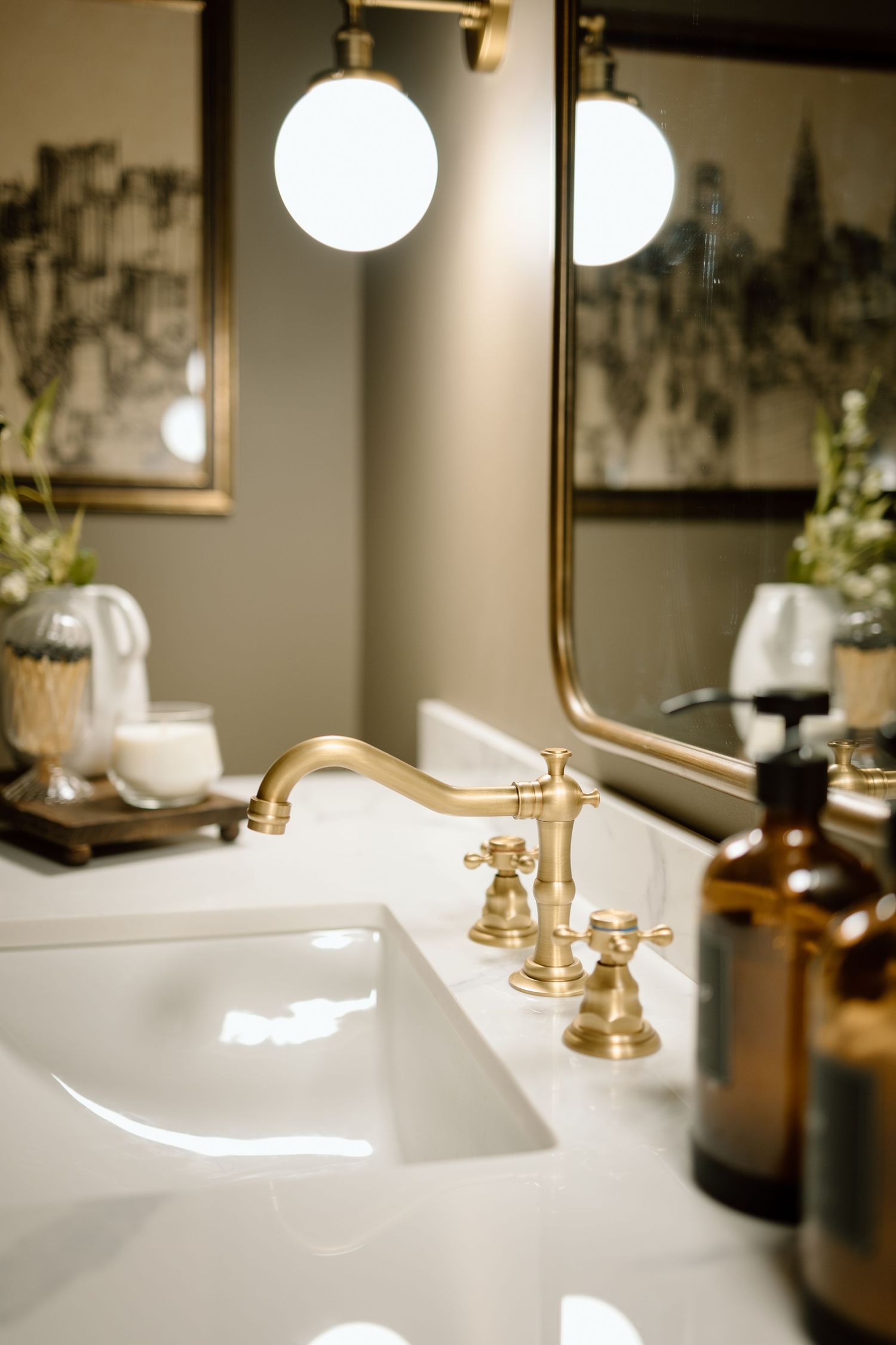 Close-up of a luxurious brass bridge faucet on white marble vanity with globe lights and mirror reflection.