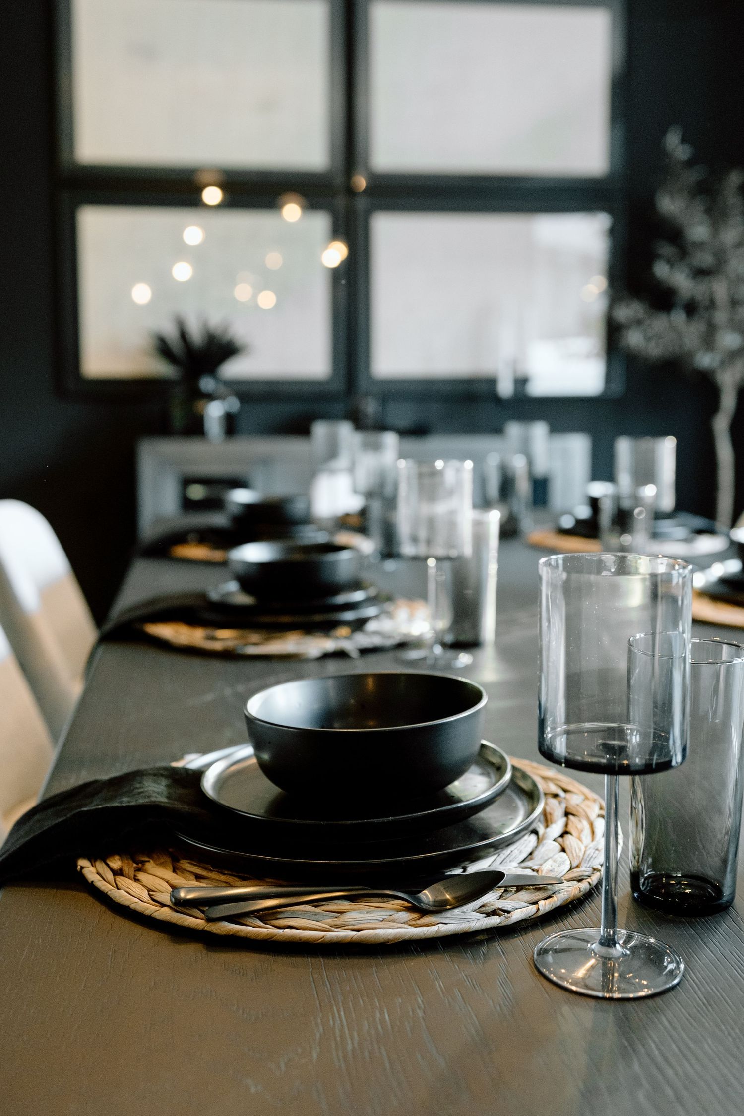 Elegant dark dining table set with black dishes, woven placemats, and glassware.