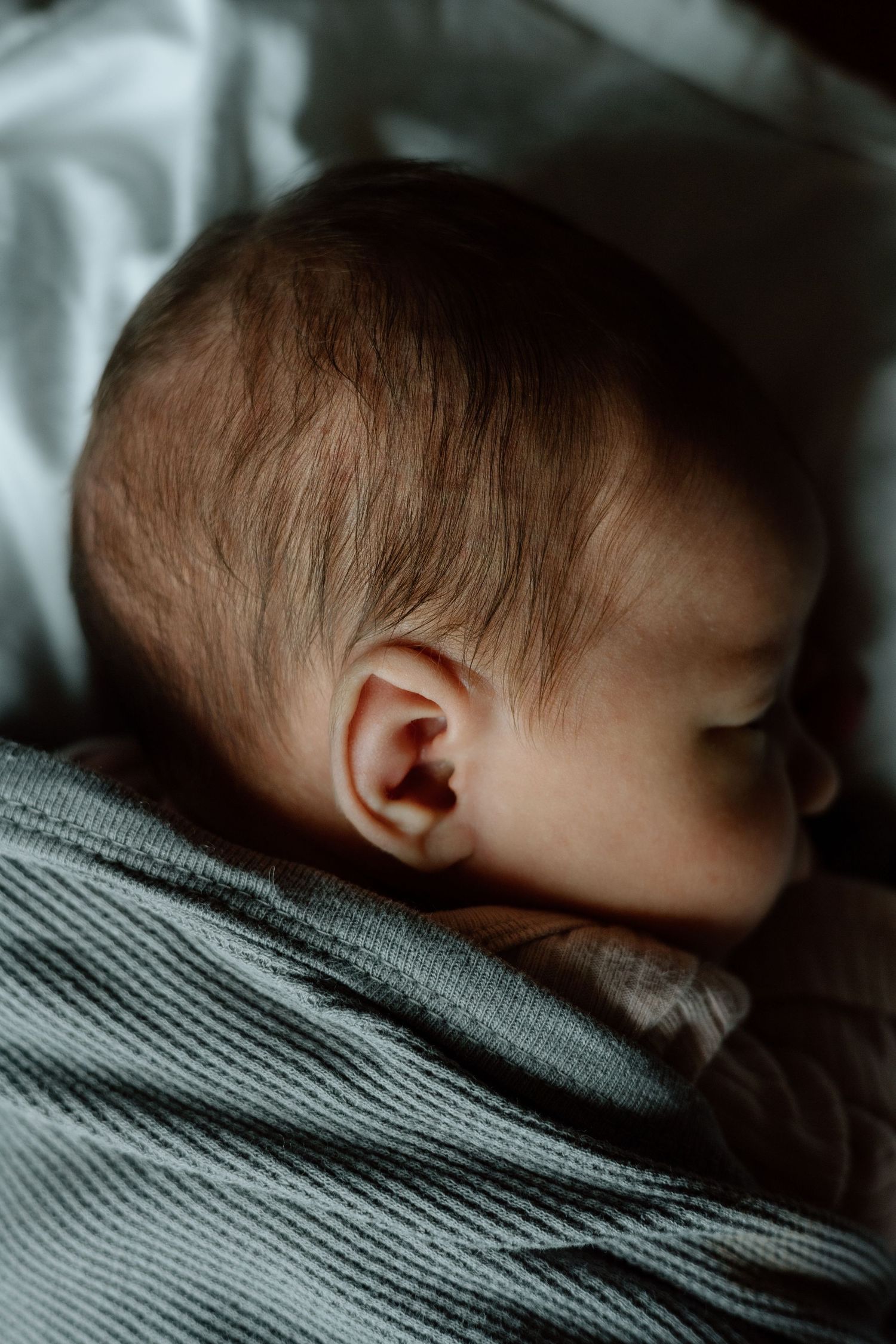 Close-up side profile of sleeping newborn baby with fine hair wrapped in teal swaddle blanket.
