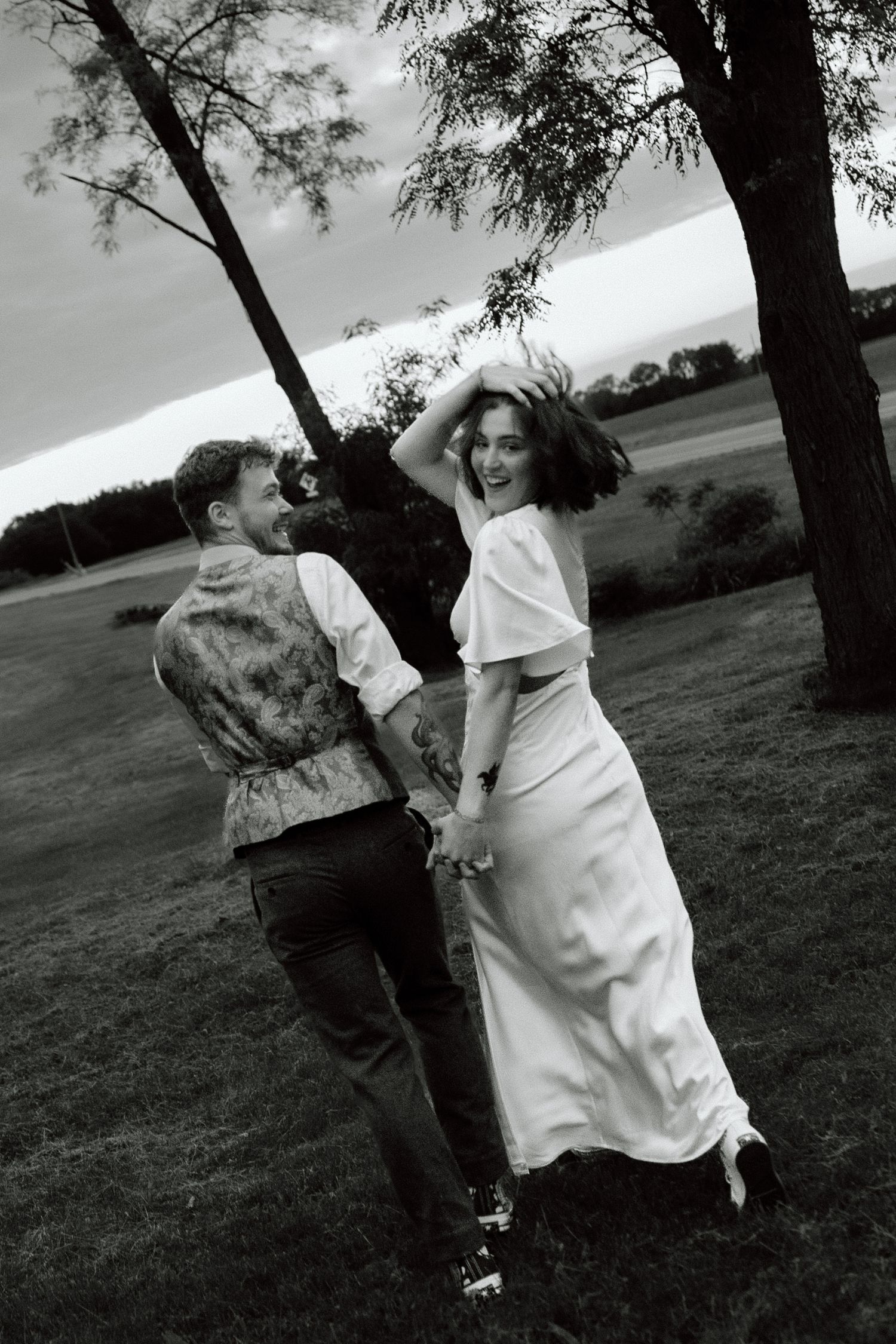 Black and white photo of bride and groom holding hands at sunset.