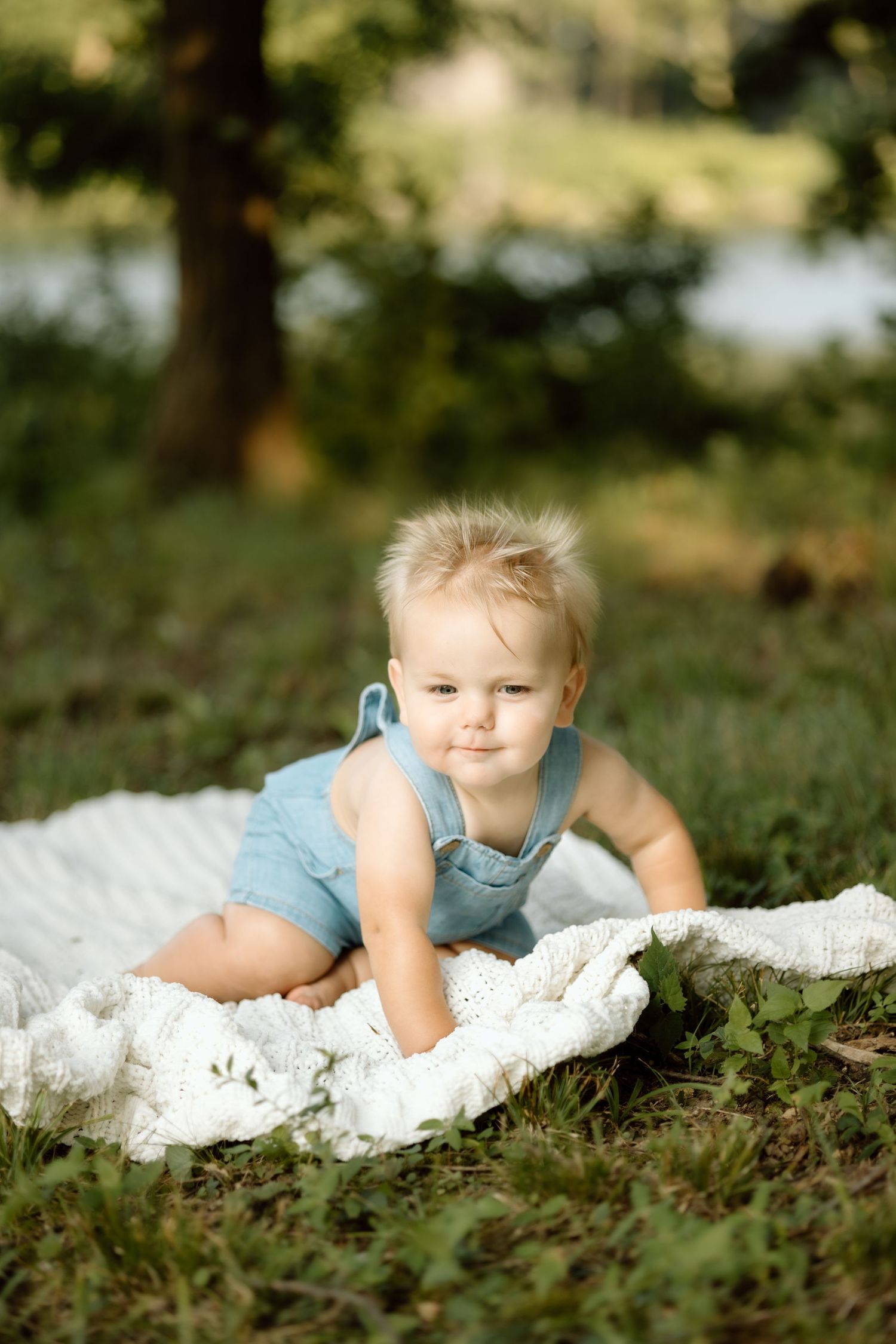Adorable baby in blue romper crawling on white blanket in sunny park.