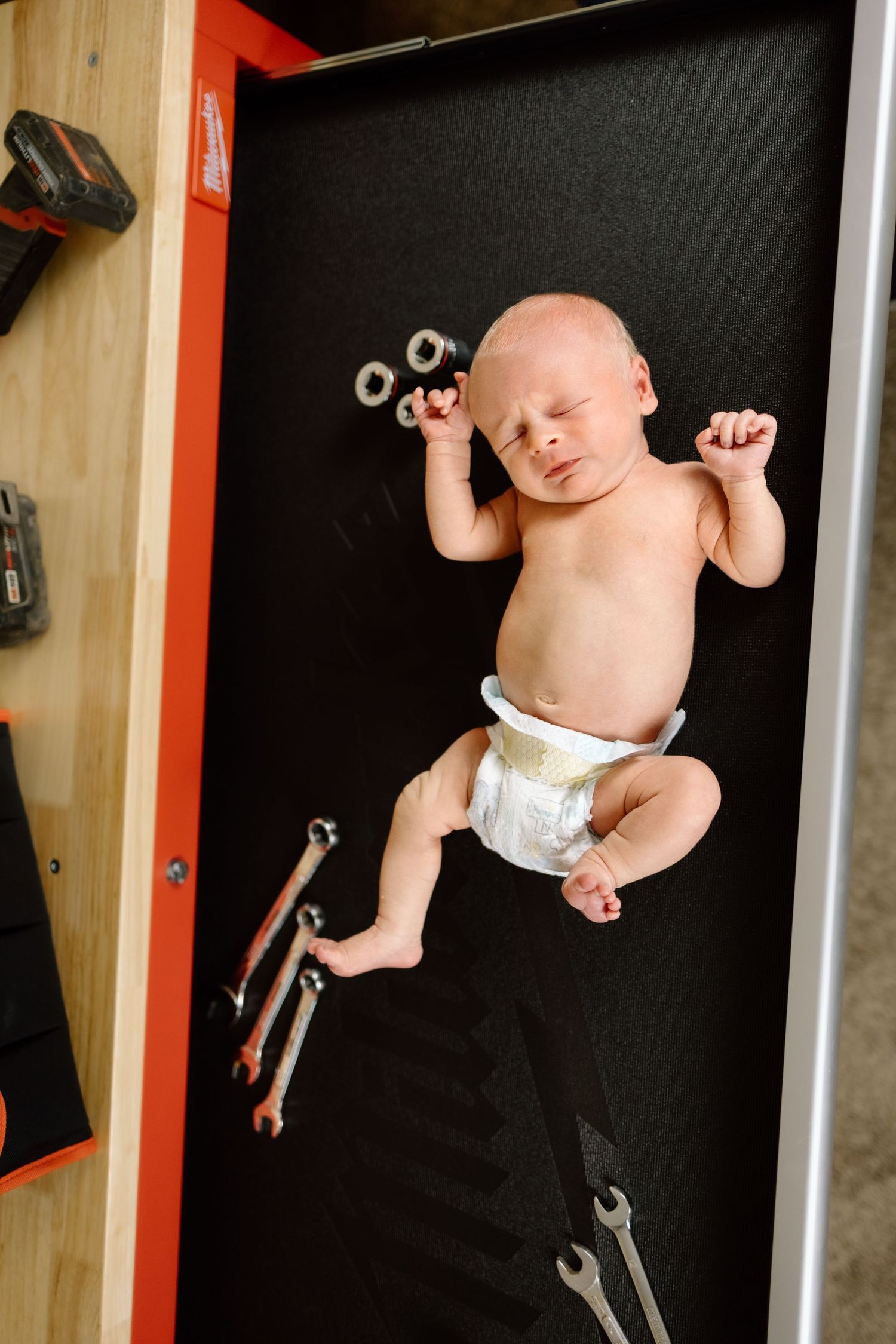 Newborn baby in diaper lying on tool workbench surrounded by wrenches and nuts for creative photo.