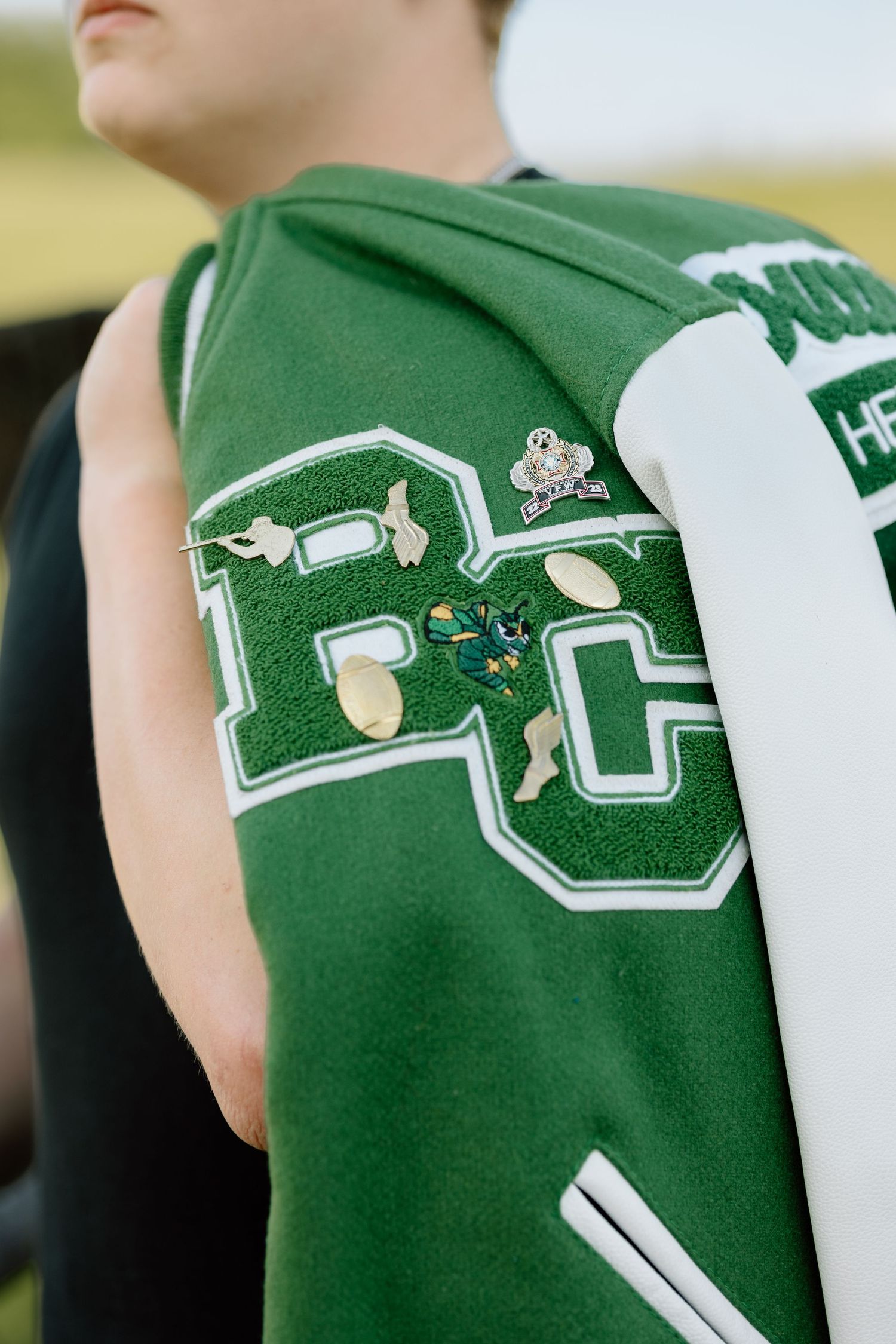 Close-up of green BC letterman jacket with pins and embroidered letters on student's back.