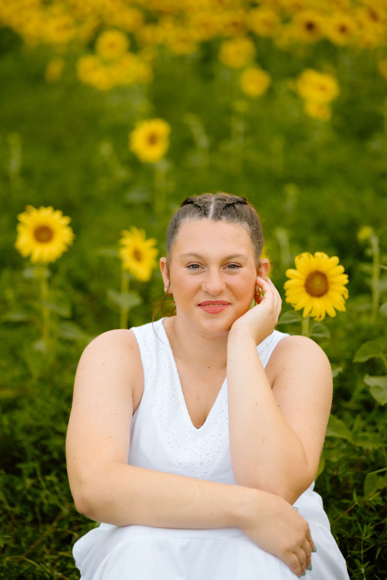 Young woman in white dress posing gracefully in a lush sunflower field on a sunny day.
