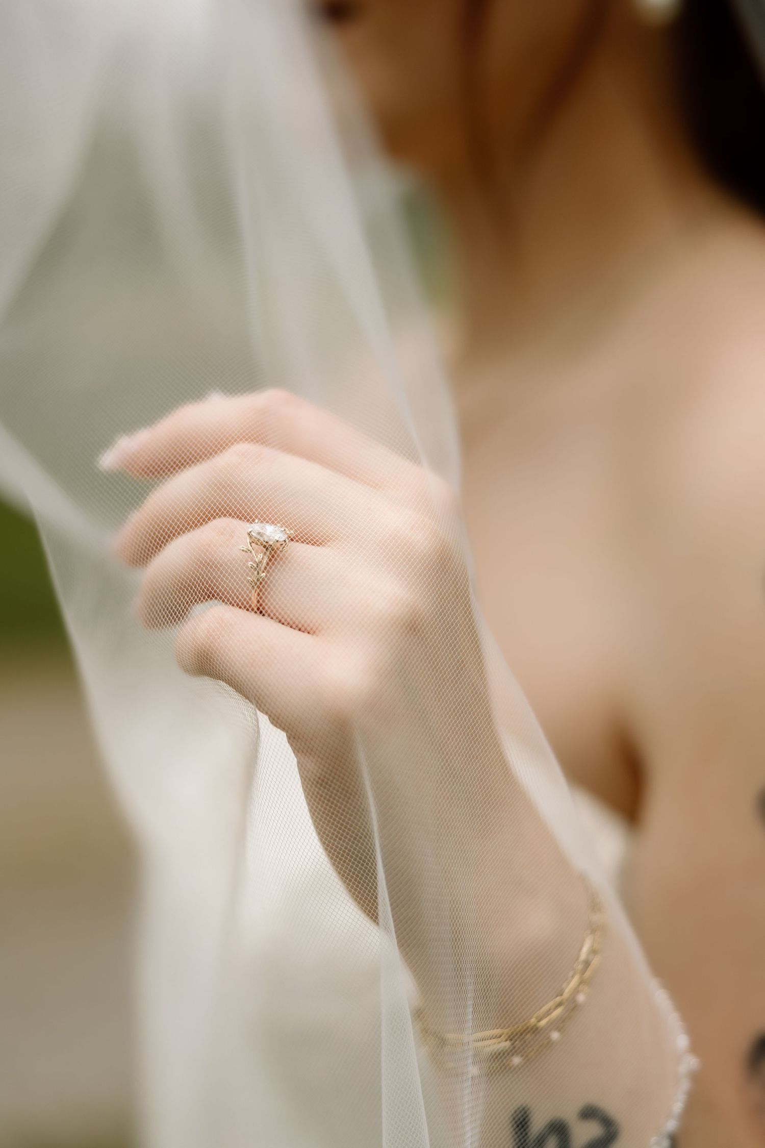 Close-up of bride's hand wearing gold engagement ring and bracelet, holding sheer wedding veil.