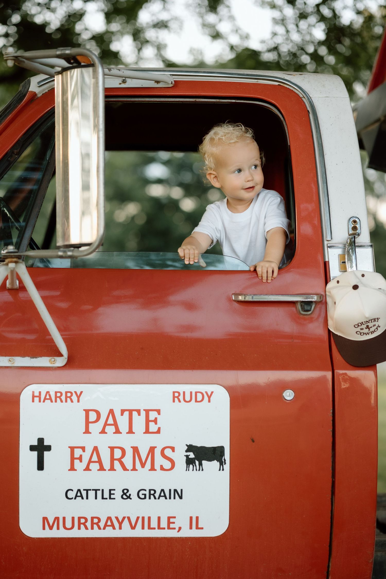 Blond toddler peeks out window of red Pate Farms cattle and grain truck in Murrayville IL.