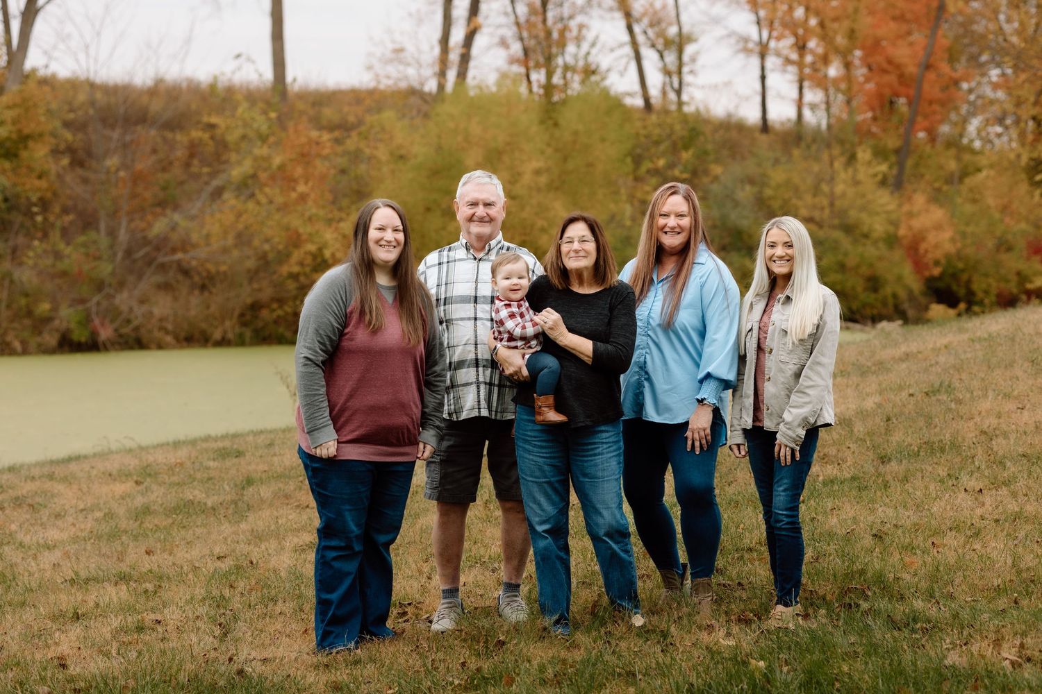 Extended family of six adults and a baby posing together in a colorful autumn outdoor setting.