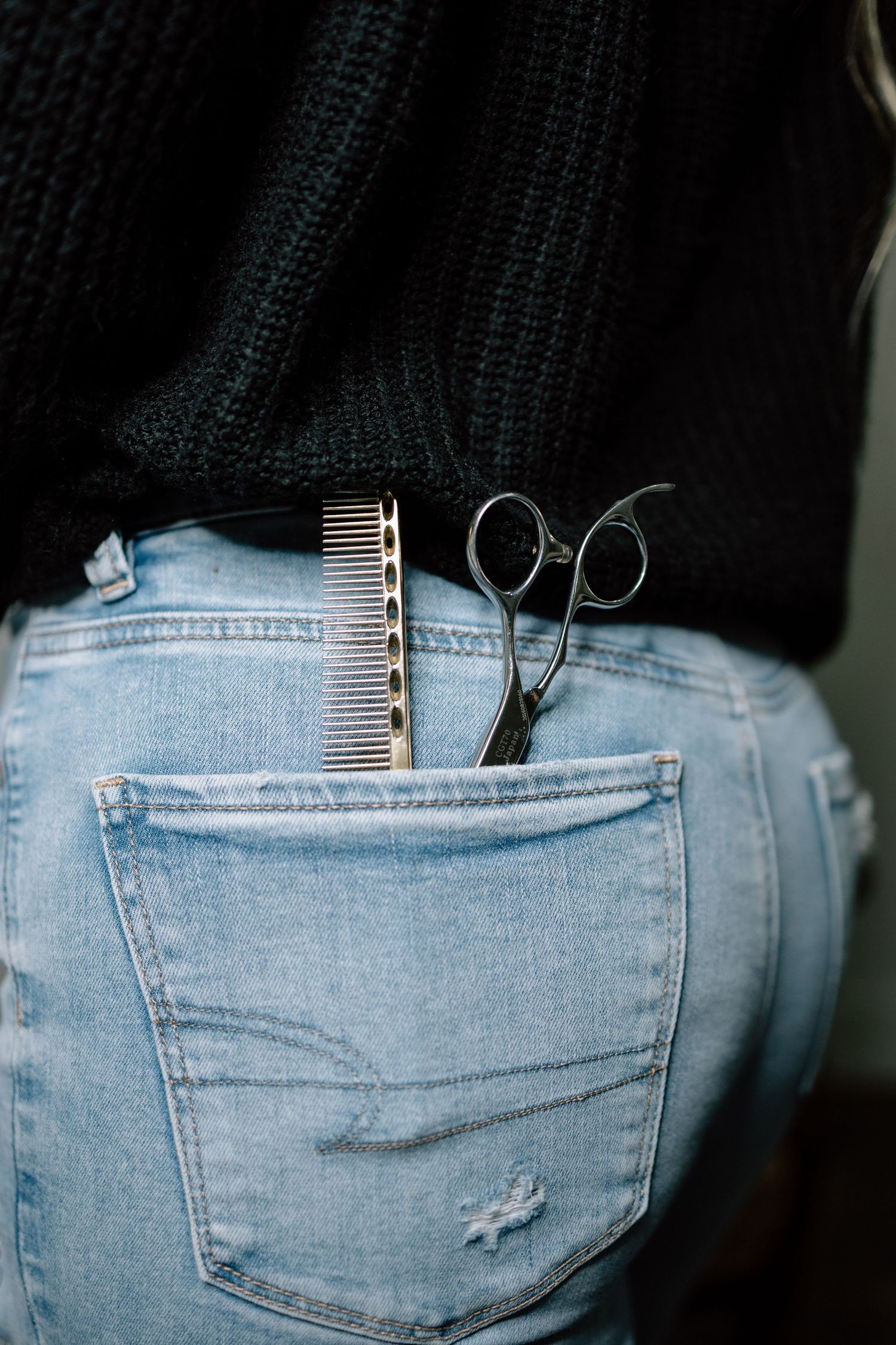 Hair scissors and a comb tucked into the back pocket of light blue distressed jeans.