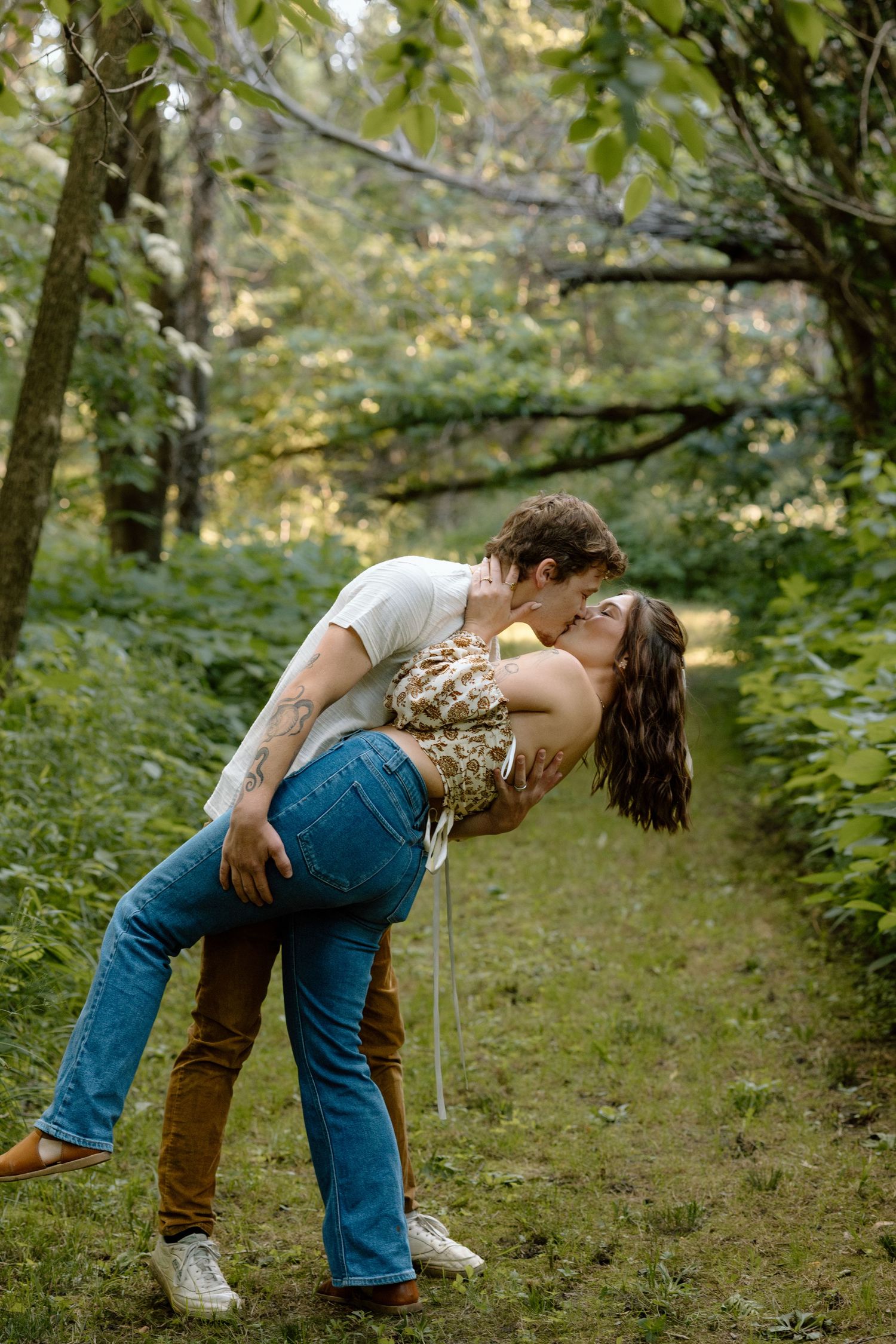 Couple sharing a romantic dip kiss on a lush green forest path.