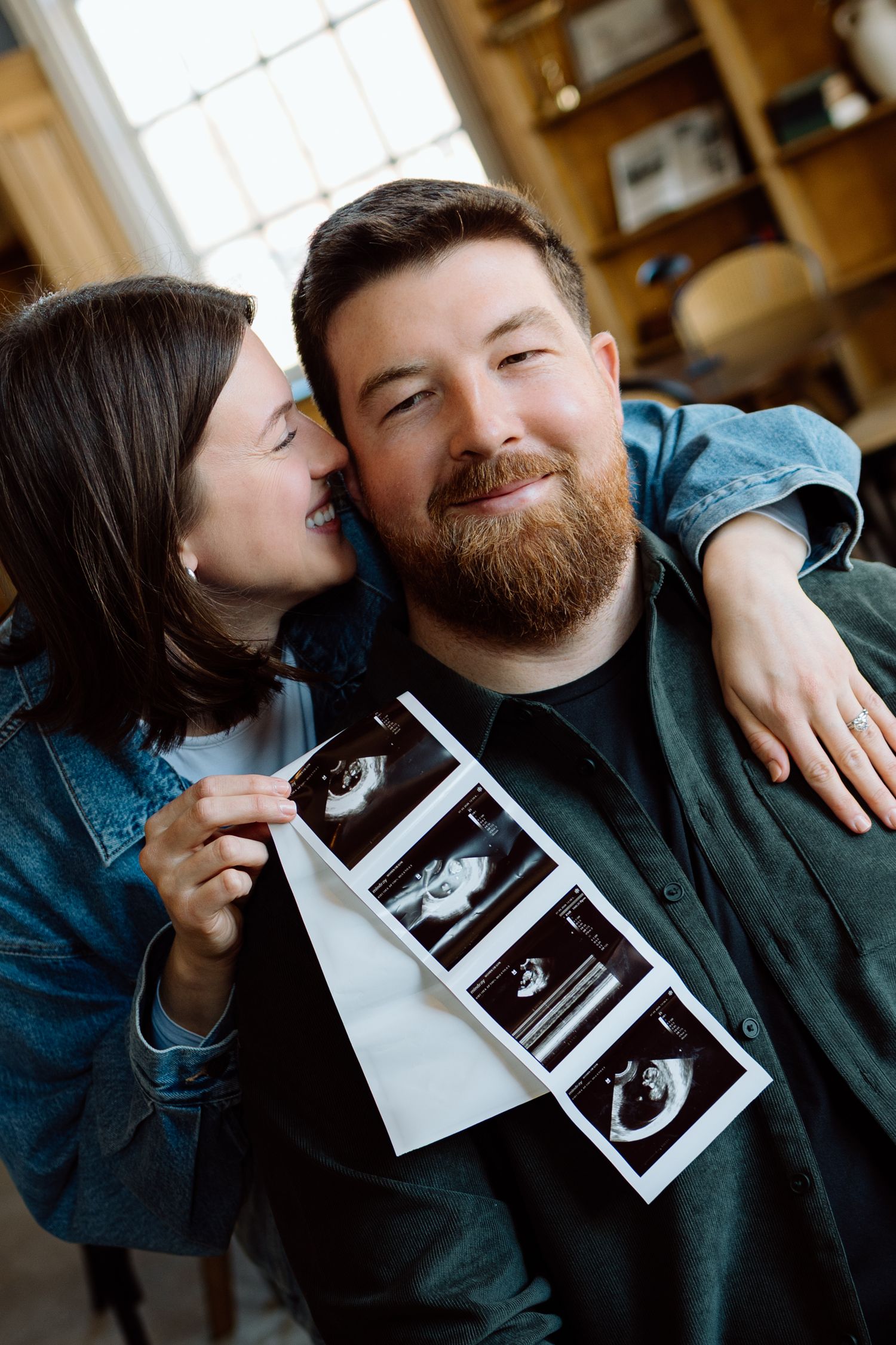 Happy couple sharing pregnancy announcement with ultrasound photos, woman kissing man's cheek.