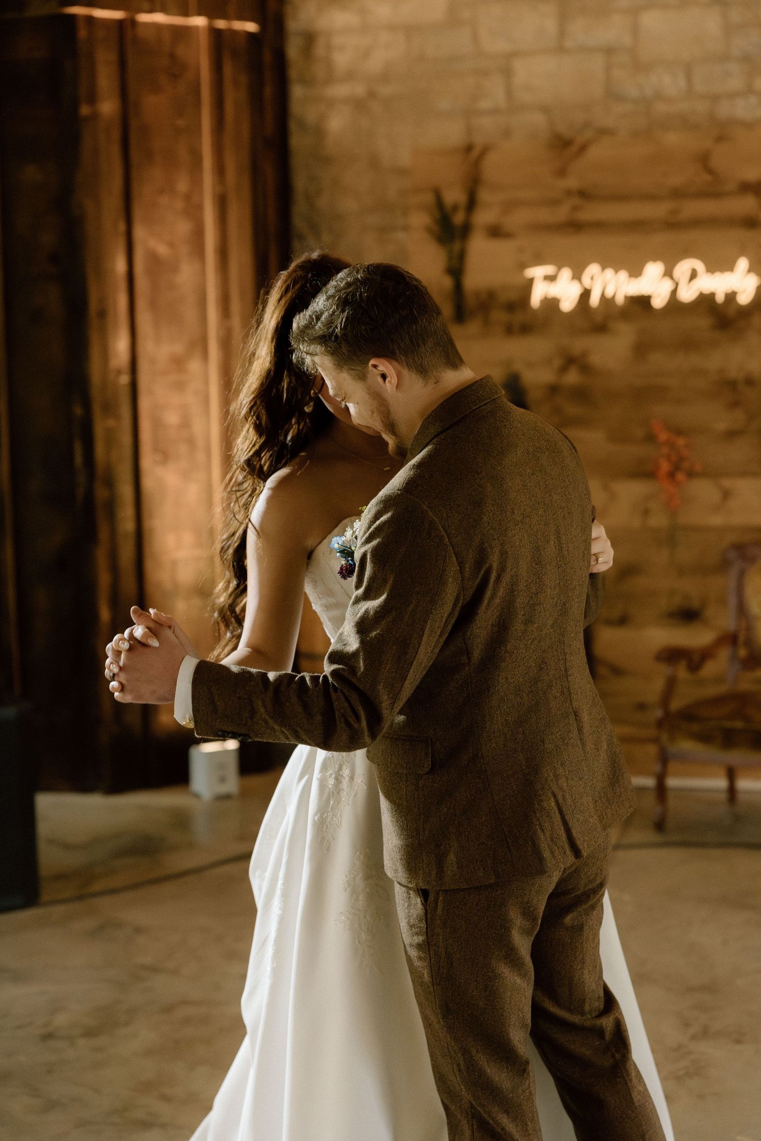 Bride and groom share intimate first dance in warmly lit barn reception hall.