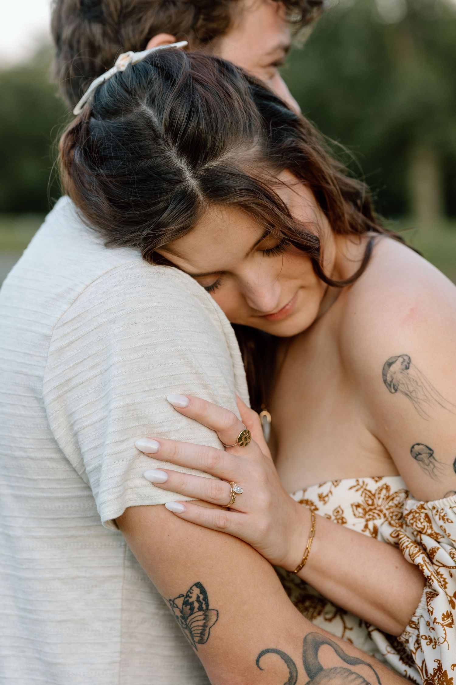 Tattooed woman tenderly hugging man's arm in a warm outdoor portrait.