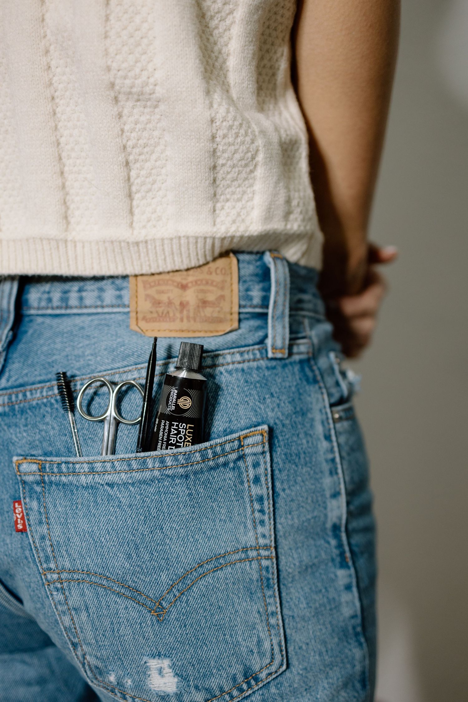Close-up of Levis jeans back pocket with scissors and hair product bottle tucked inside.