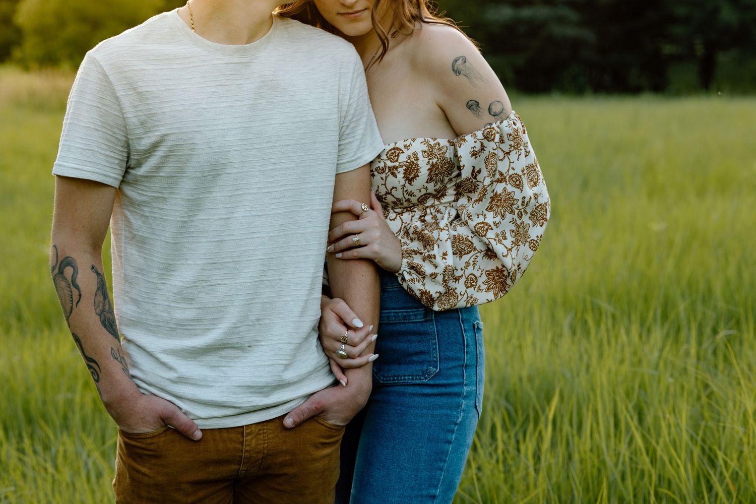 Close-up of tattooed couple embracing intimately in a green grassy field.