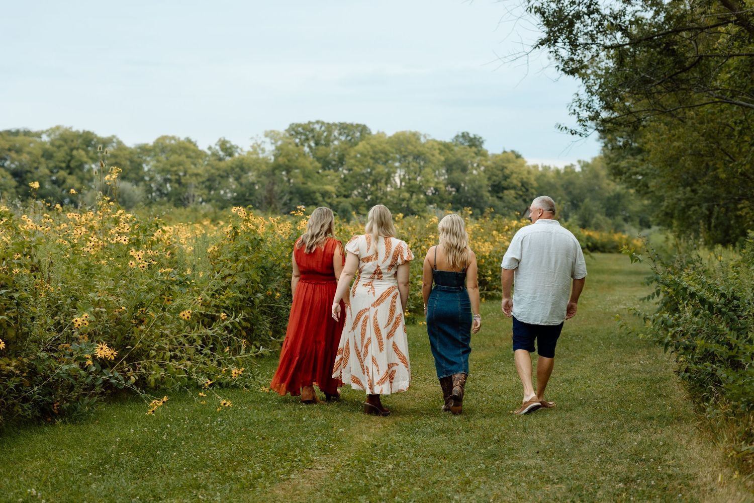 Family of four walking together along a scenic path bordered by vibrant yellow wildflowers.