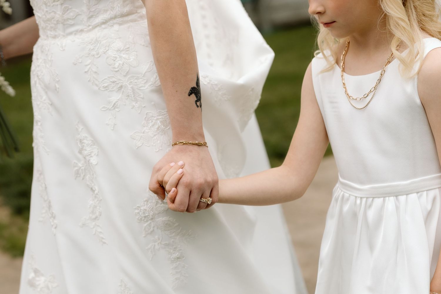 Close-up of bride with horse tattoo holding hands with young flower girl in white dress.