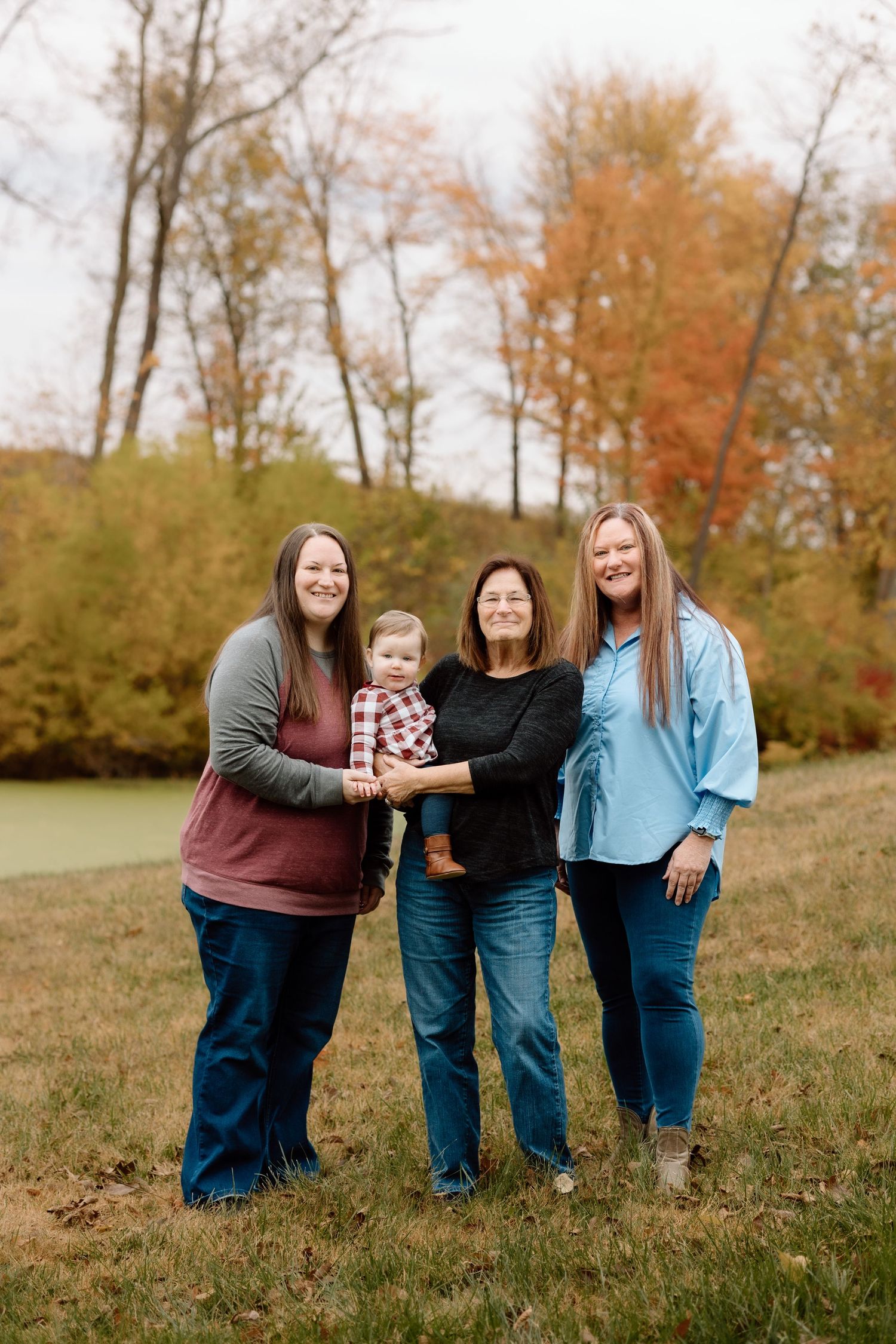 Four women and a baby posing together for a multigenerational family portrait in an autumn landscape.