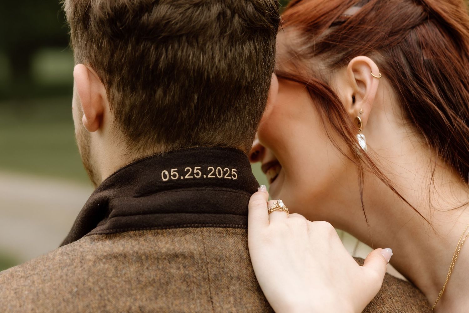Close-up of groom's collar embroidered with wedding date 05.25.2025 as bride embraces him.