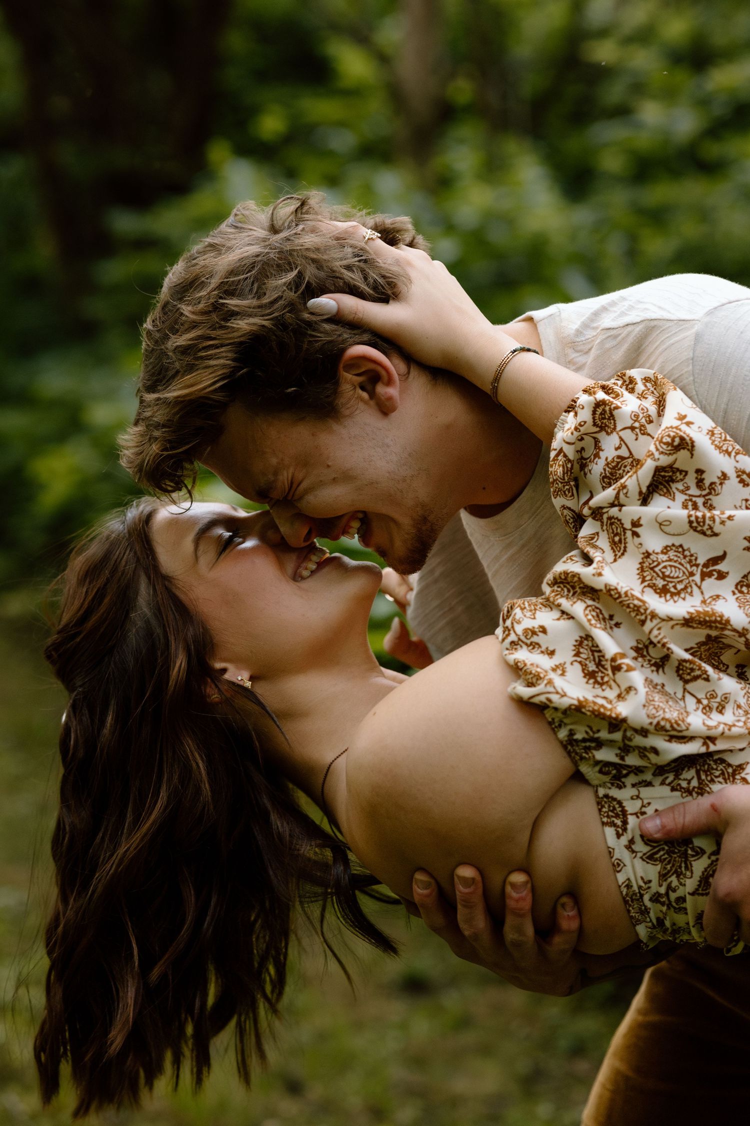 Couple sharing a passionate dip kiss surrounded by lush green foliage outdoors.