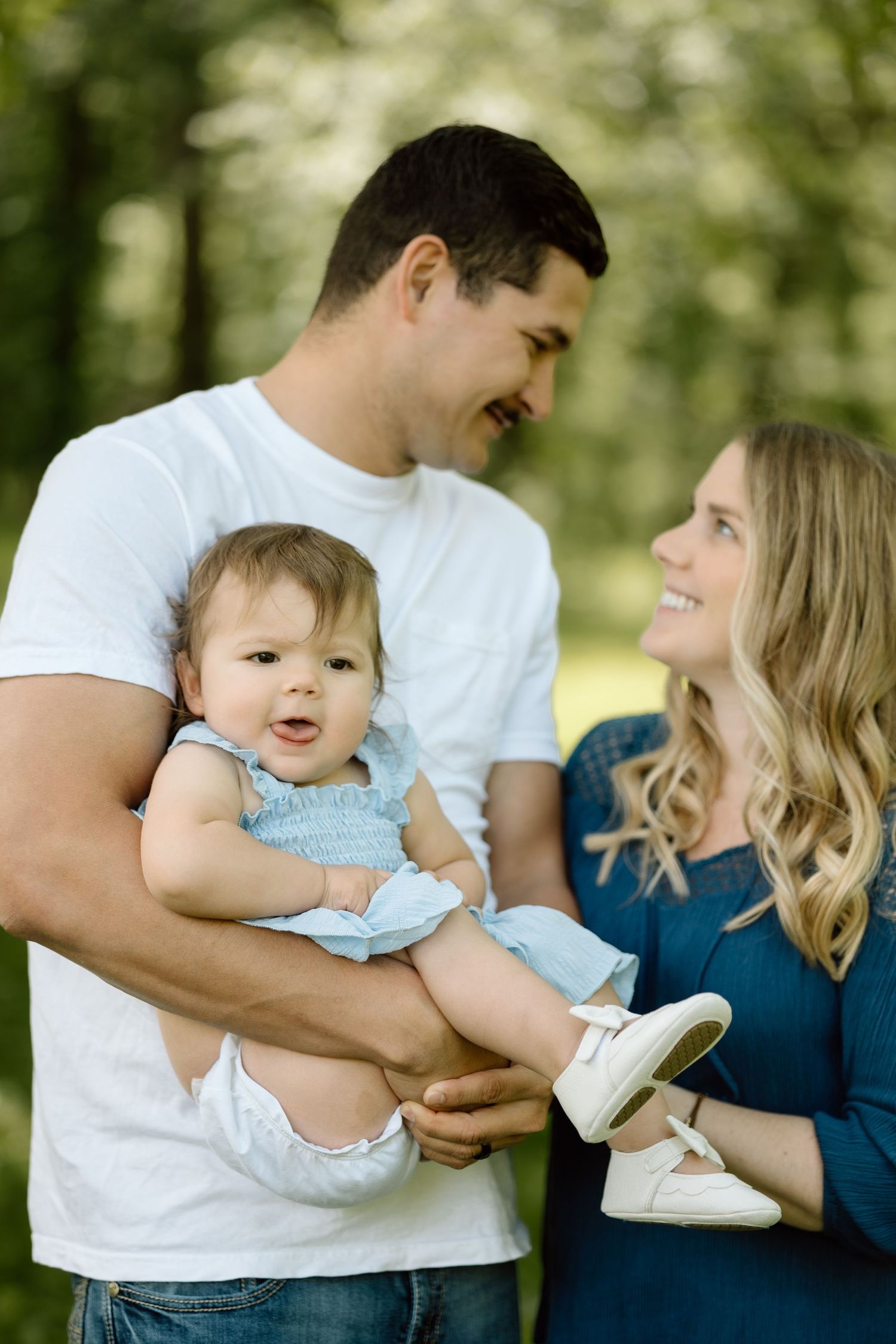 Happy parents share a tender moment with their baby daughter in a blue dress during an outdoor photo session.