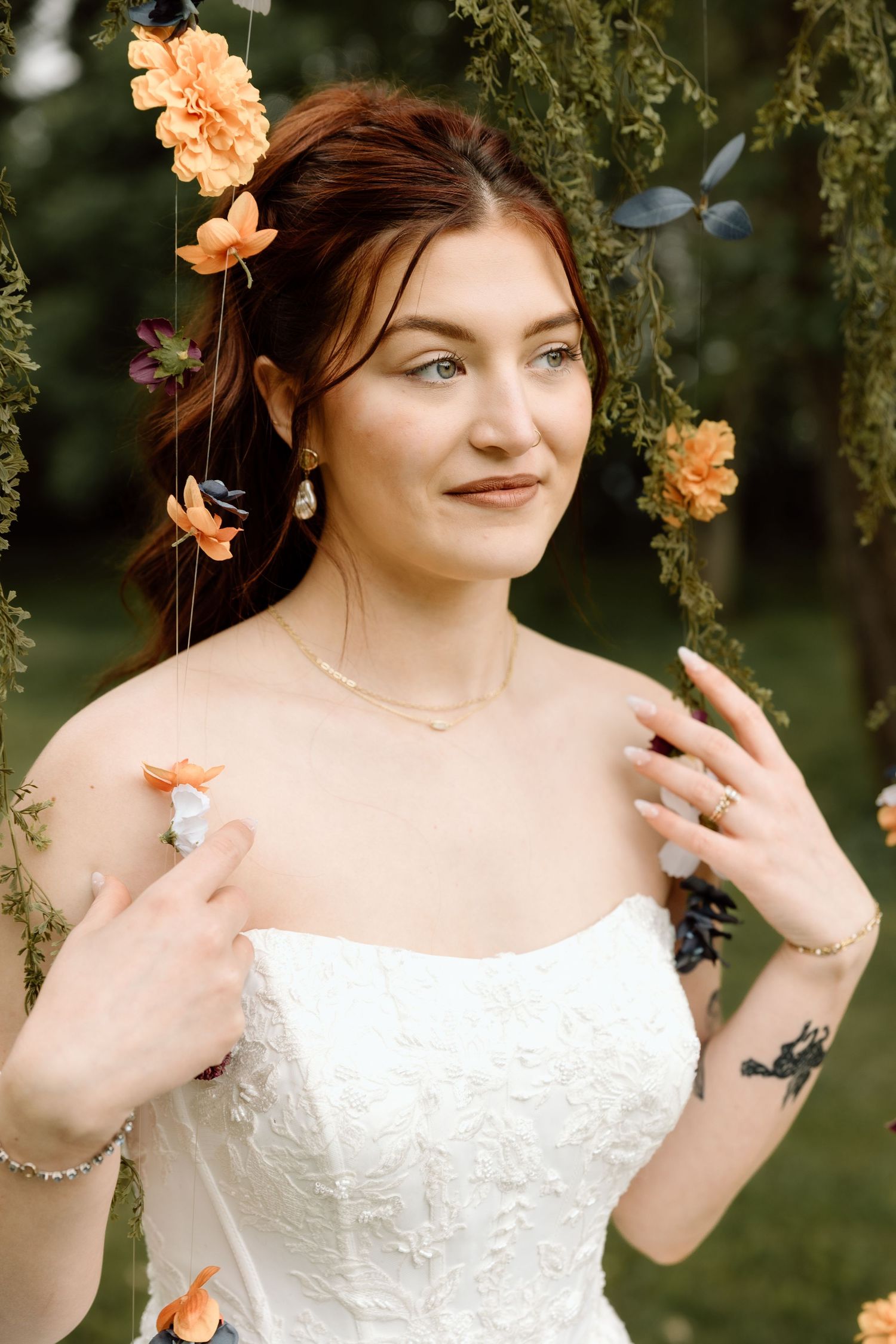 Beautiful red-haired bride in white strapless gown surrounded by orange flowers in a garden setting.