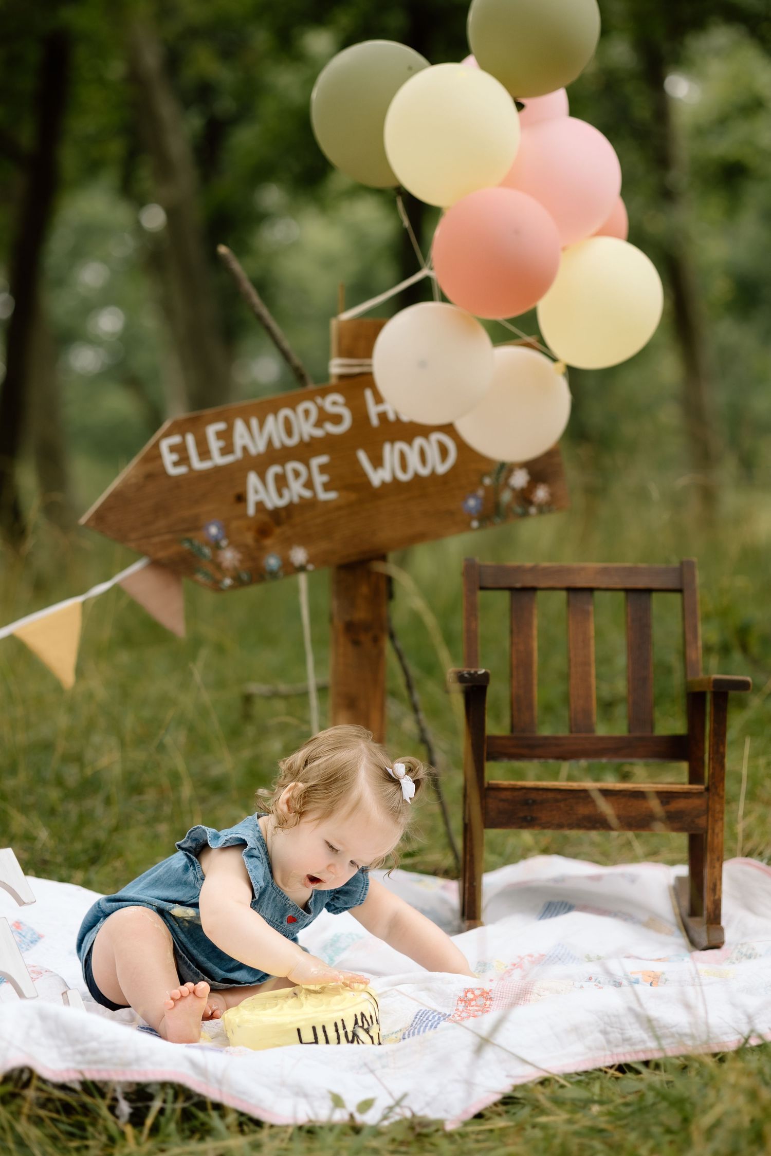 Baby girl in denim dress reaching for birthday cake at Winnie the Pooh themed outdoor party.