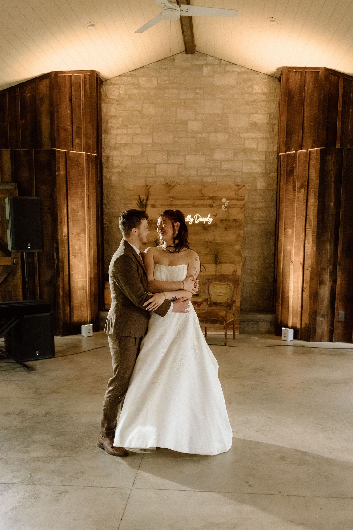 Newlyweds share romantic first dance in elegant barn venue with neon sign backdrop.