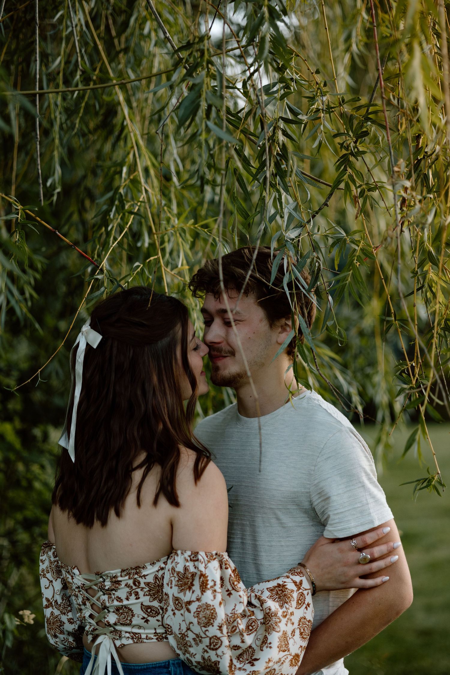 Couple sharing a kiss under weeping willow tree branches in a garden.