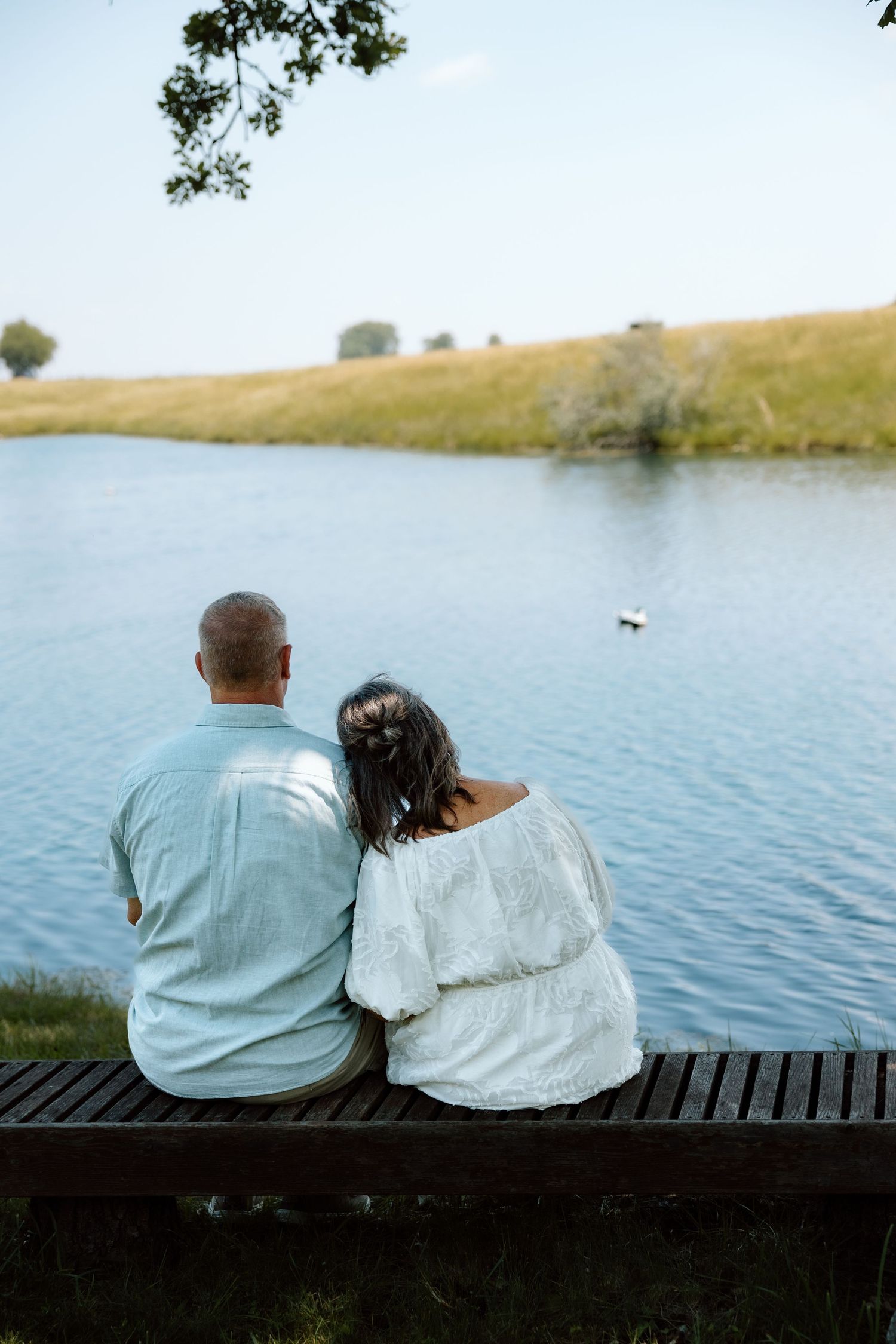 Couple sitting together on a bench overlooking a serene pond in nature.