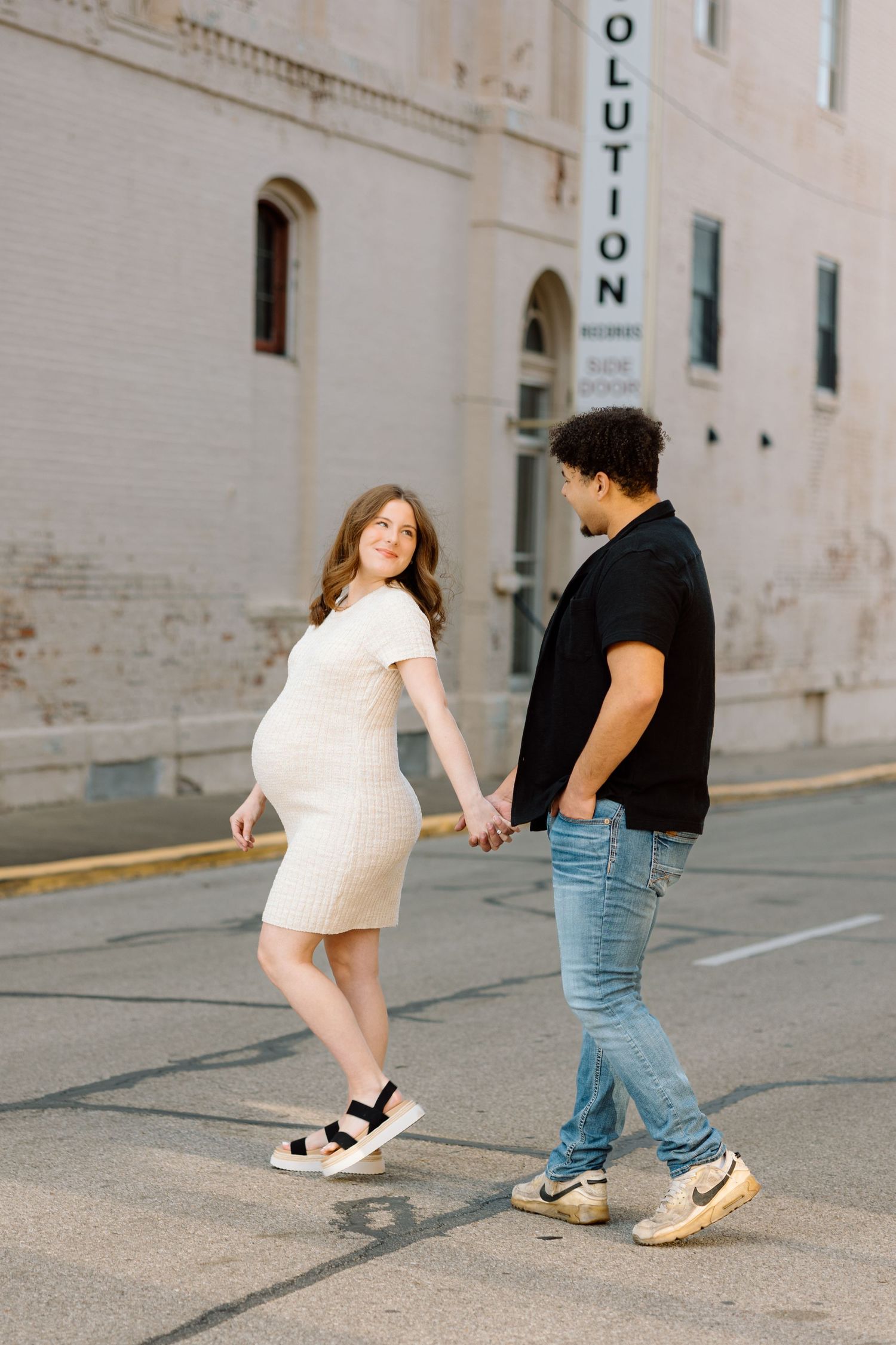 Pregnant couple holding hands and walking together near a historic building during outdoor maternity shoot.