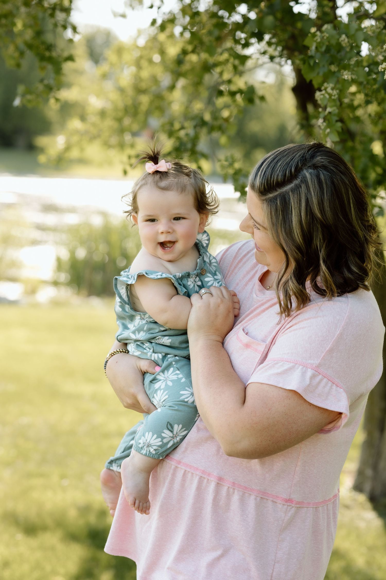 Mom gazes lovingly at her giggling baby girl in a floral romper during a golden hour outdoor photo session.
