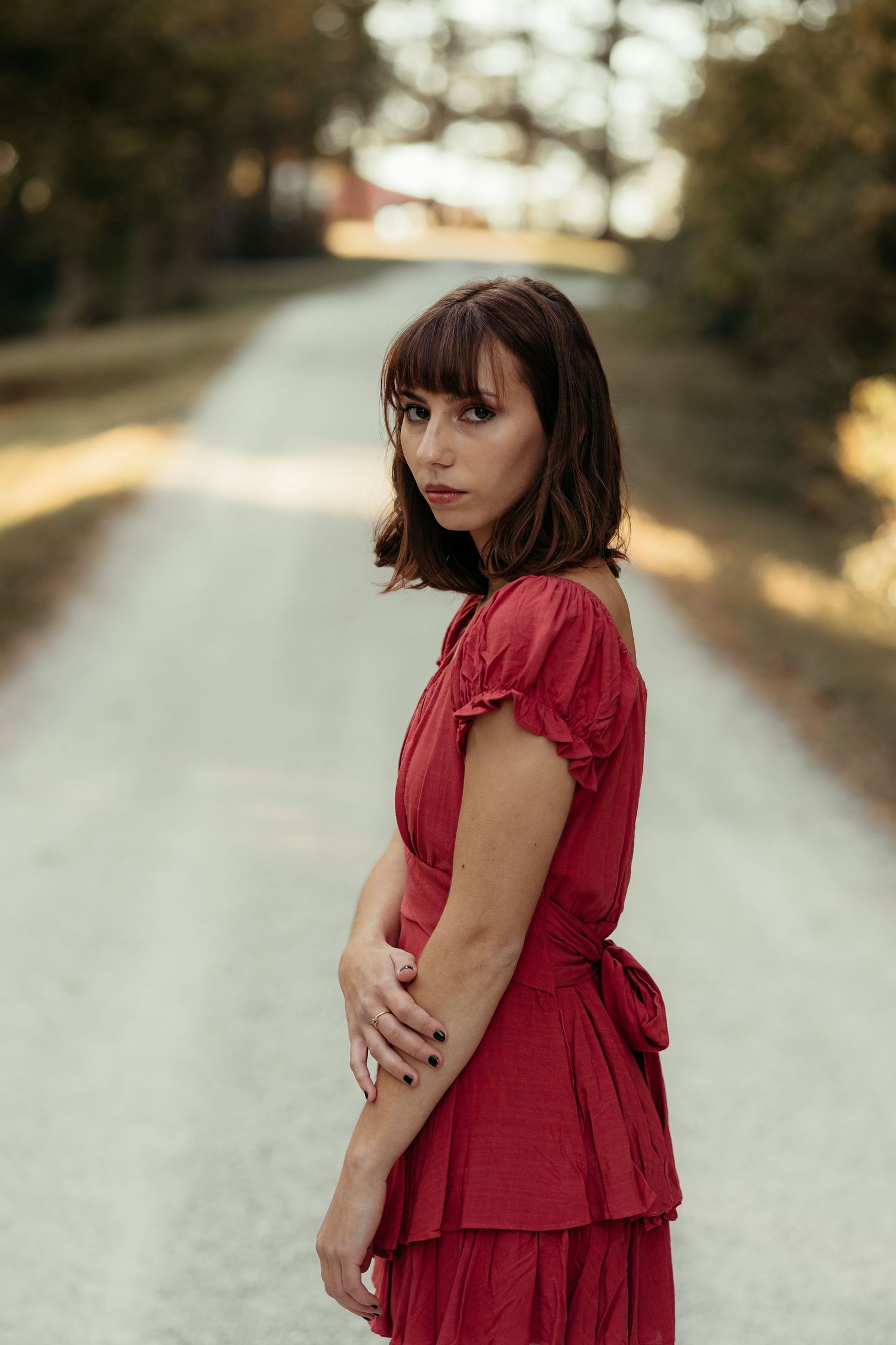 Young woman in red dress standing on a rural road at golden hour.
