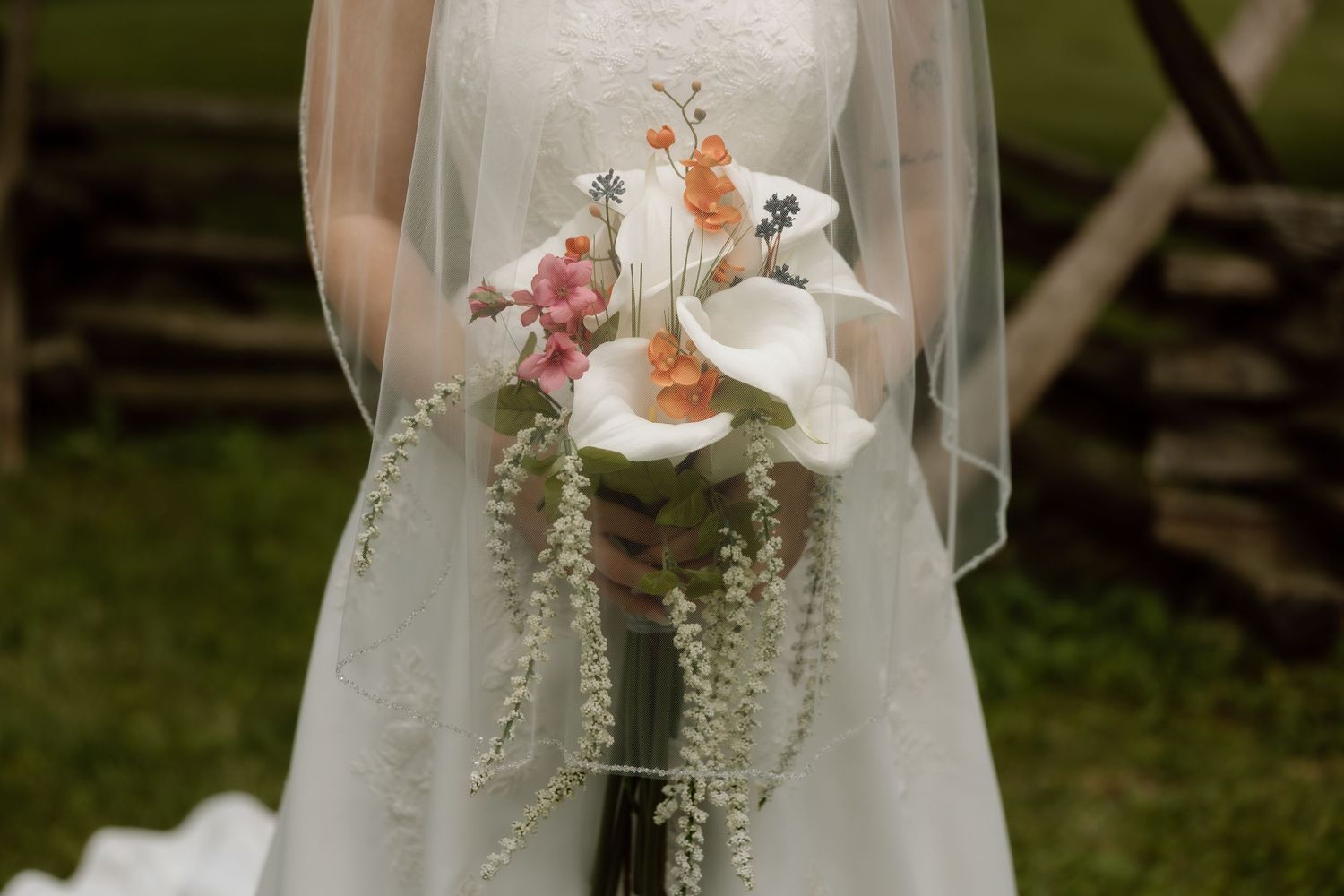 Bride in white lace gown holding cascading bouquet of calla lilies and pink flowers with veil.