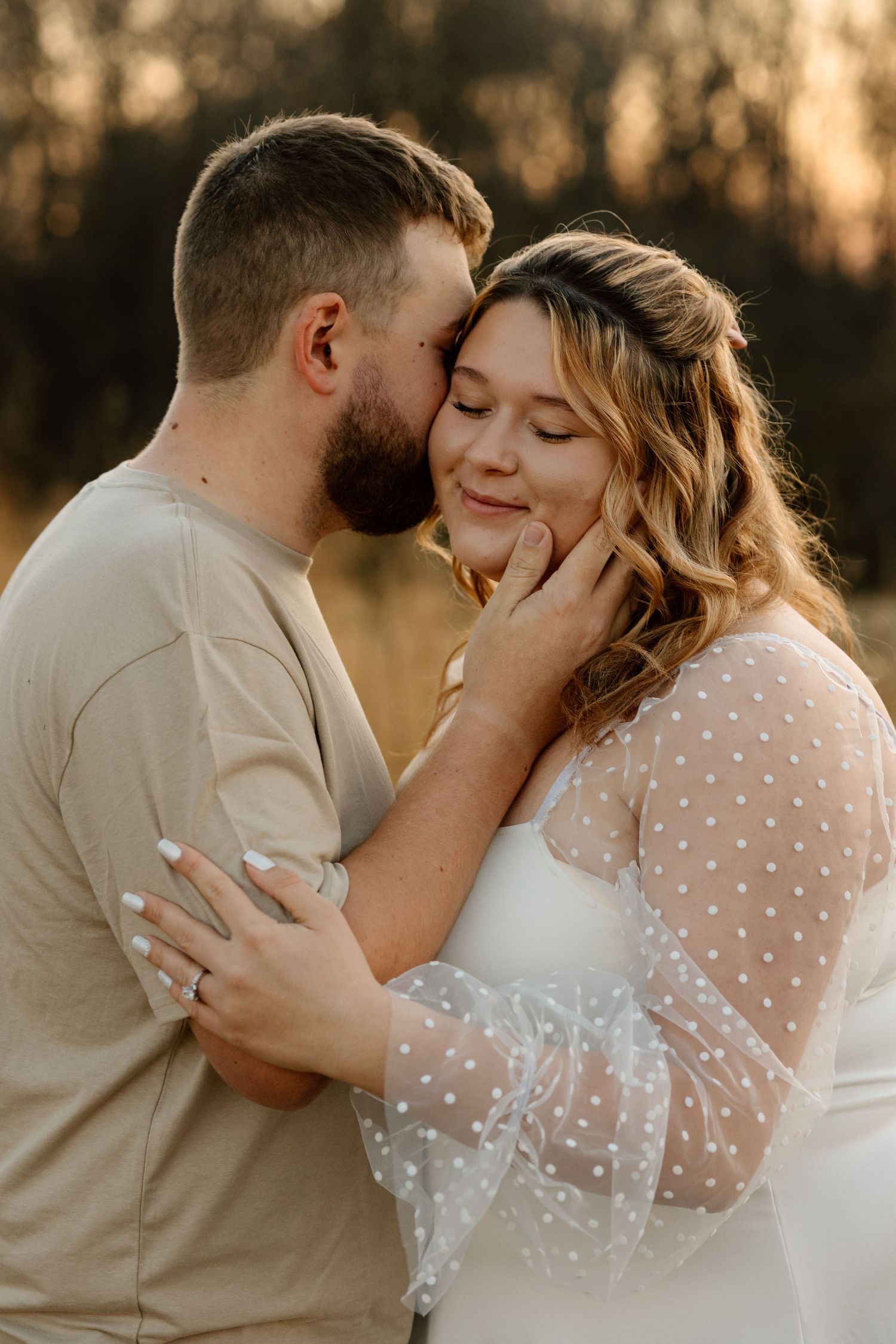 Man gently cups womans face about to kiss her cheek during romantic outdoor engagement session at sunset.