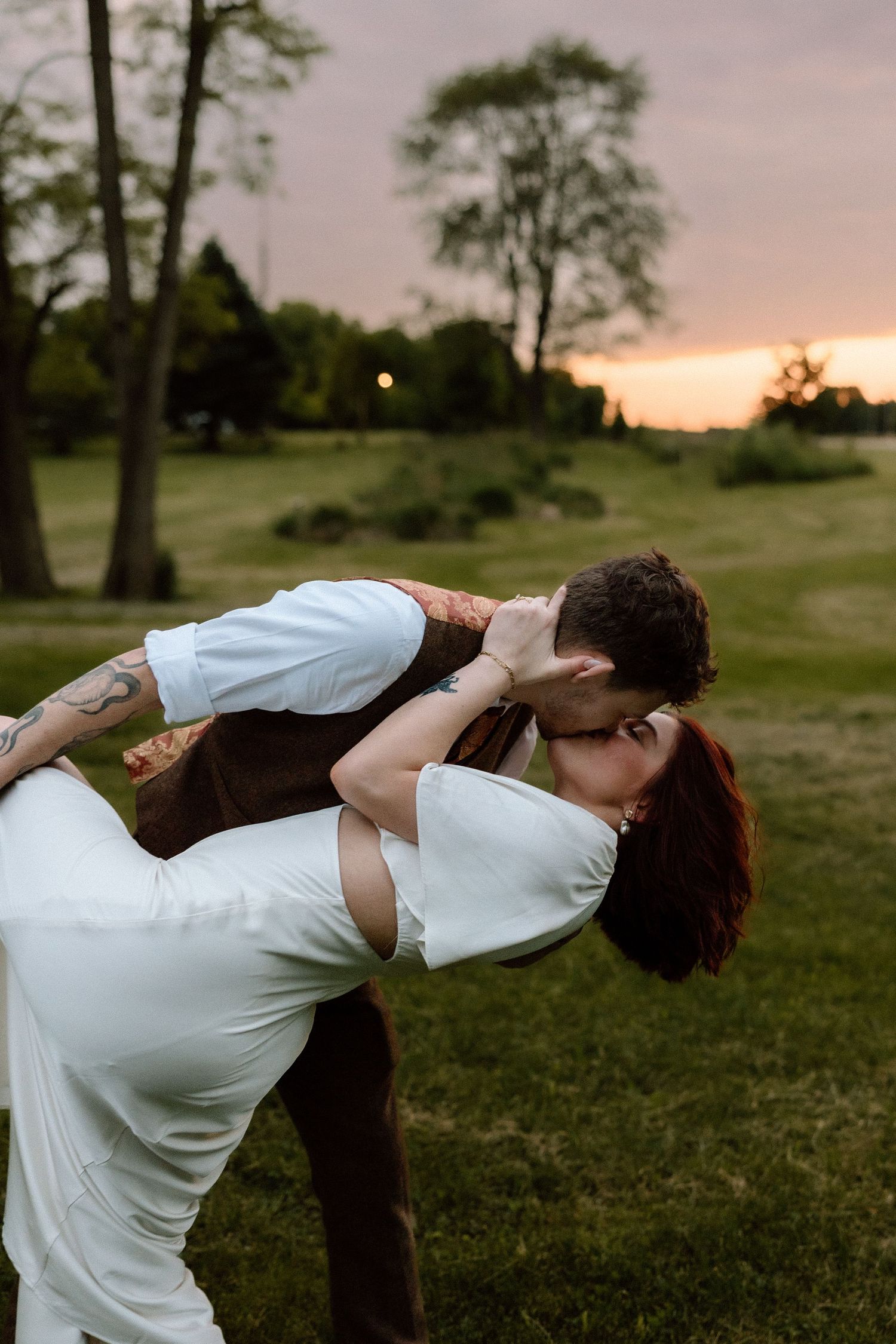 Groom dips bride for romantic kiss at golden hour sunset wedding photo.