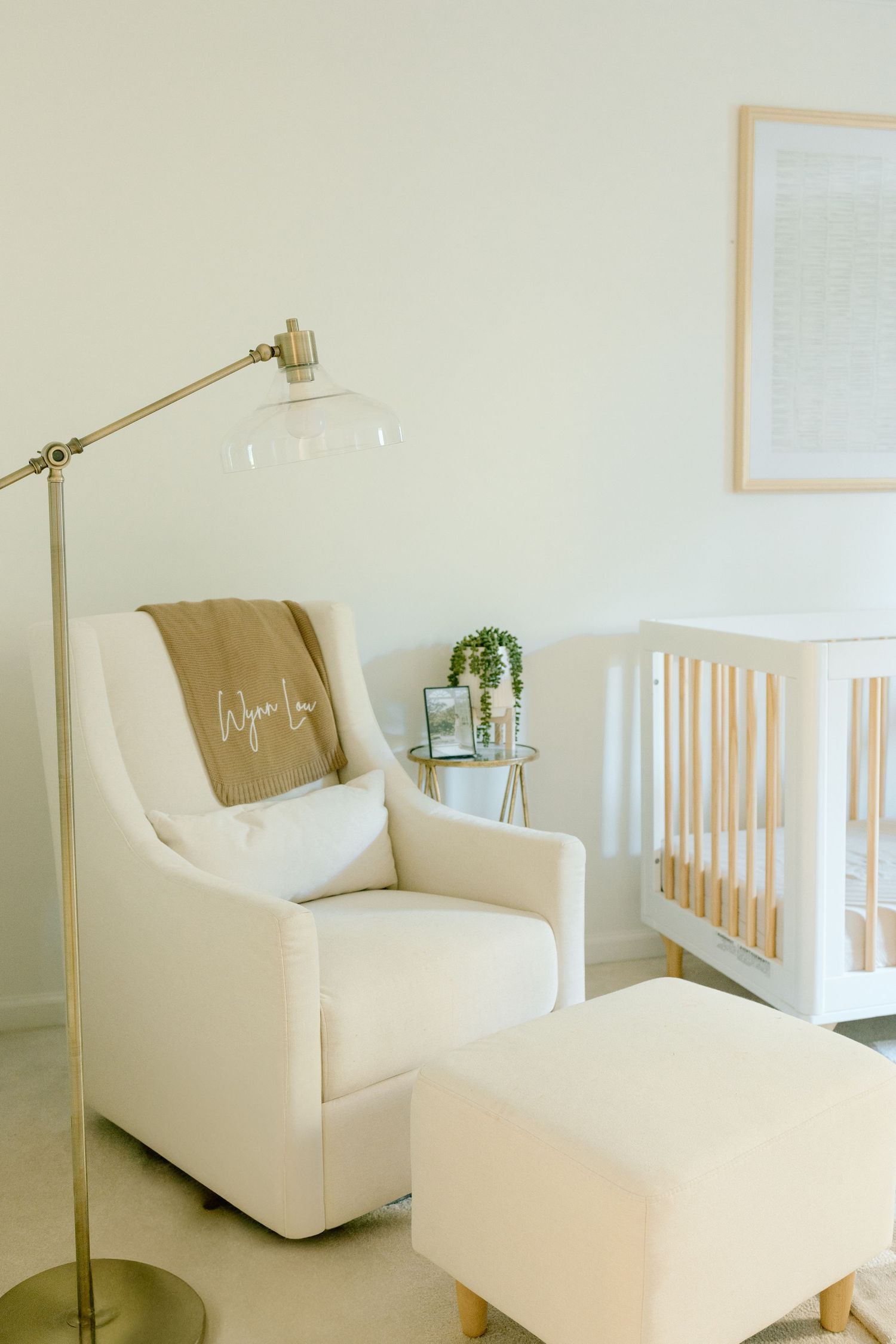 Serene nursery with cream glider chair, brass floor lamp, and white crib.