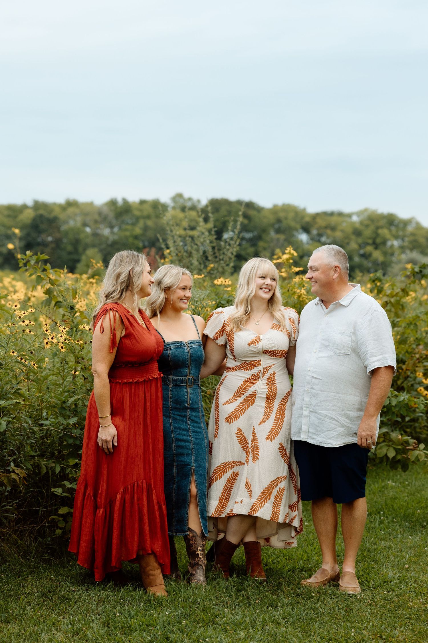 Family of four laughing and enjoying time together in a golden wildflower meadow outdoors.