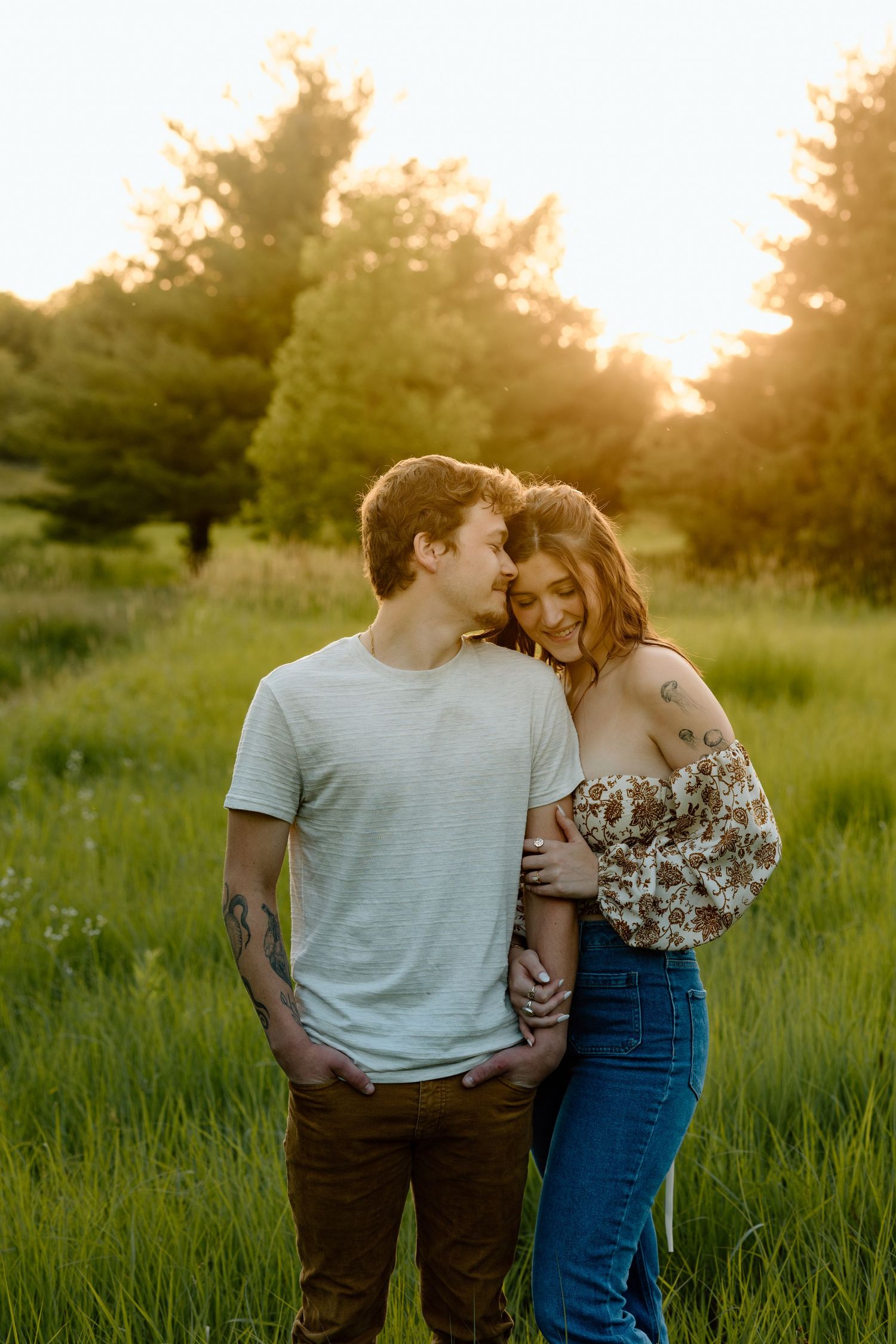 Romantic couple cuddling and smiling together in a sunlit meadow at dusk.