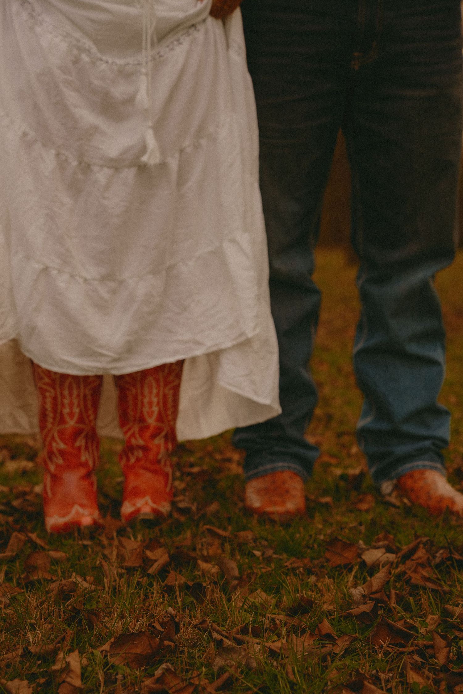 Close-up of bride in white dress wearing red cowboy boots standing beside groom in jeans.