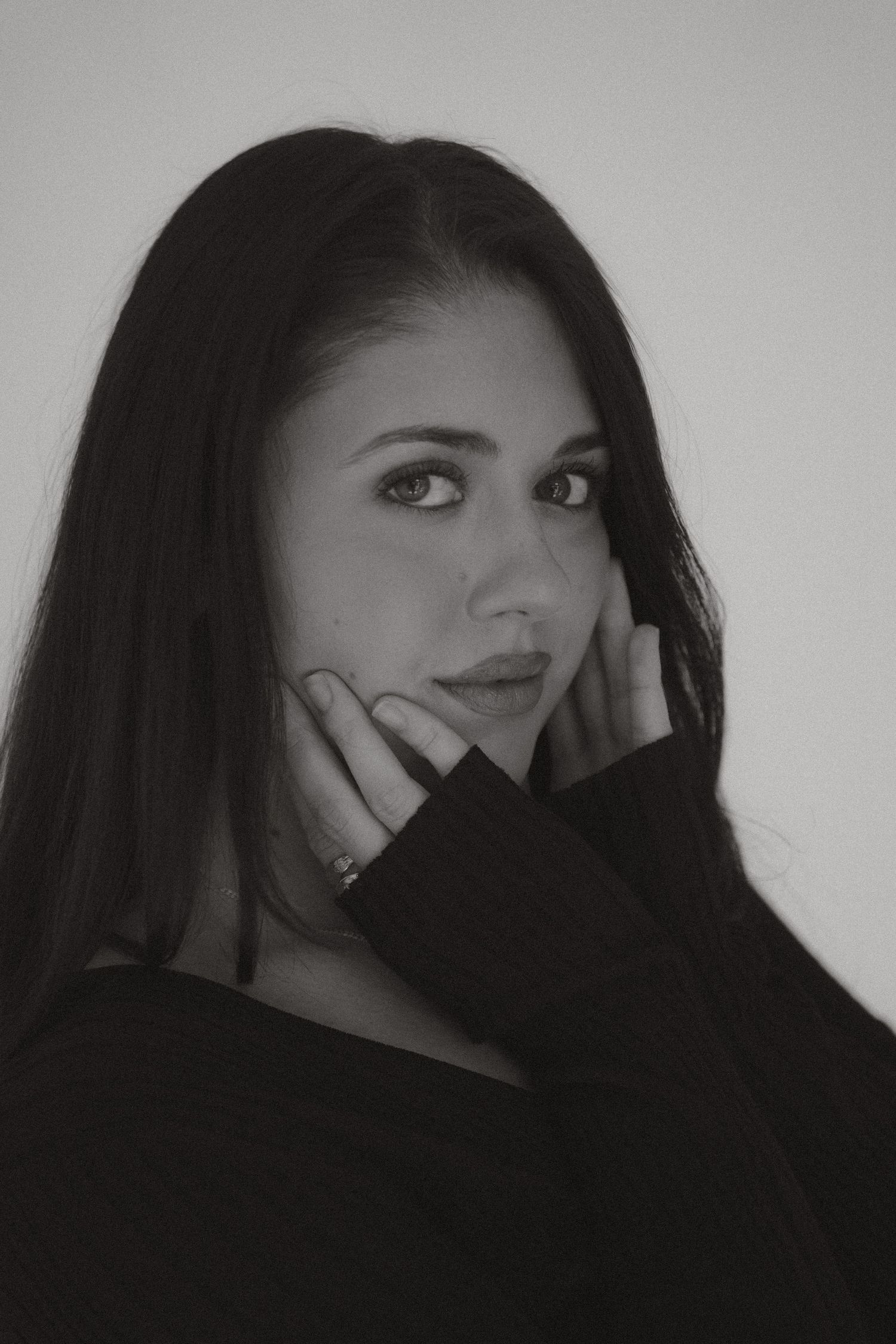 Black and white portrait of a young woman with long dark hair posing with hand near face.
